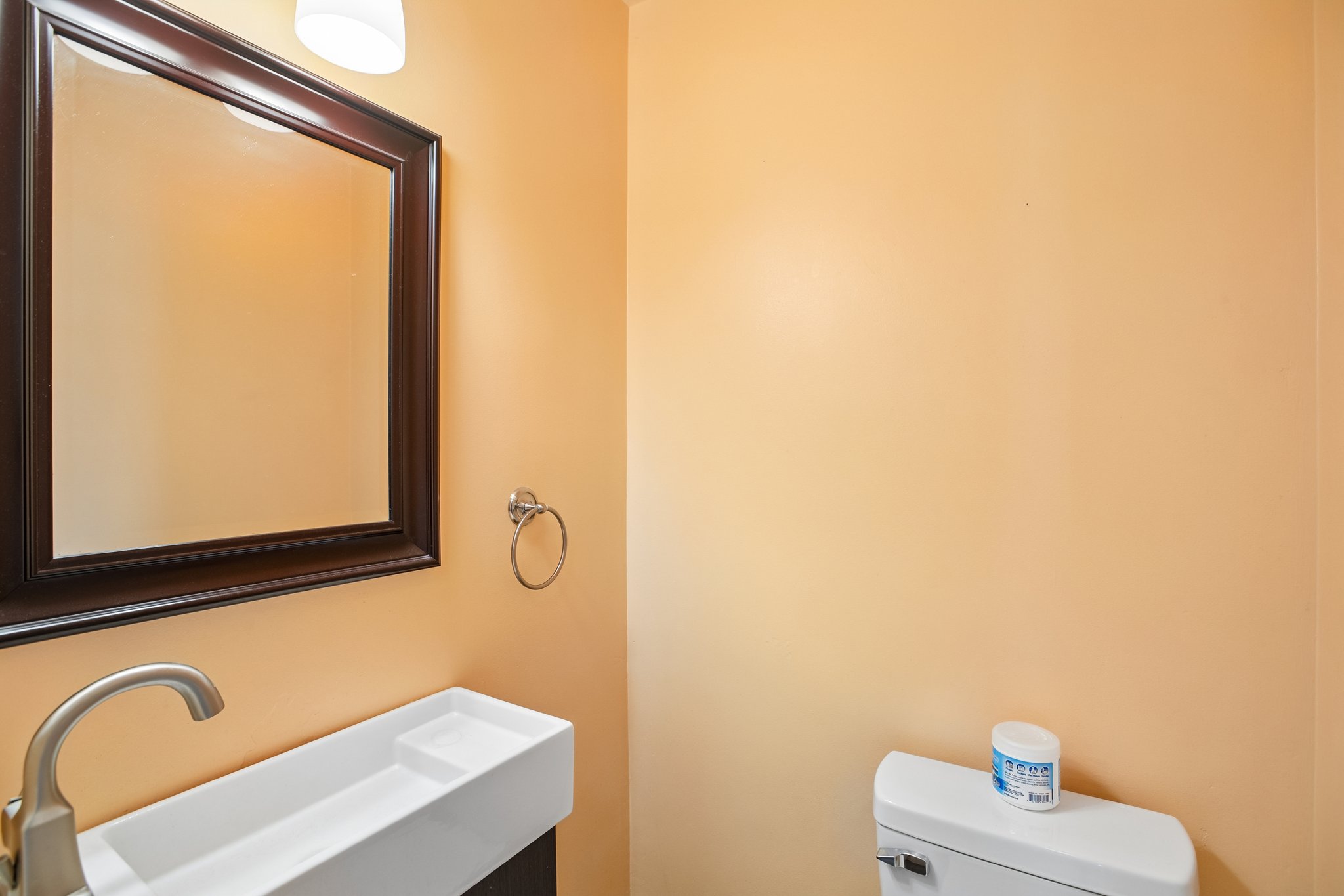Bathroom featuring a rectangular mirror with a dark wood frame, a modern wall-mounted sink, a single-handle brushed nickel faucet, and a wall-mounted light fixture
