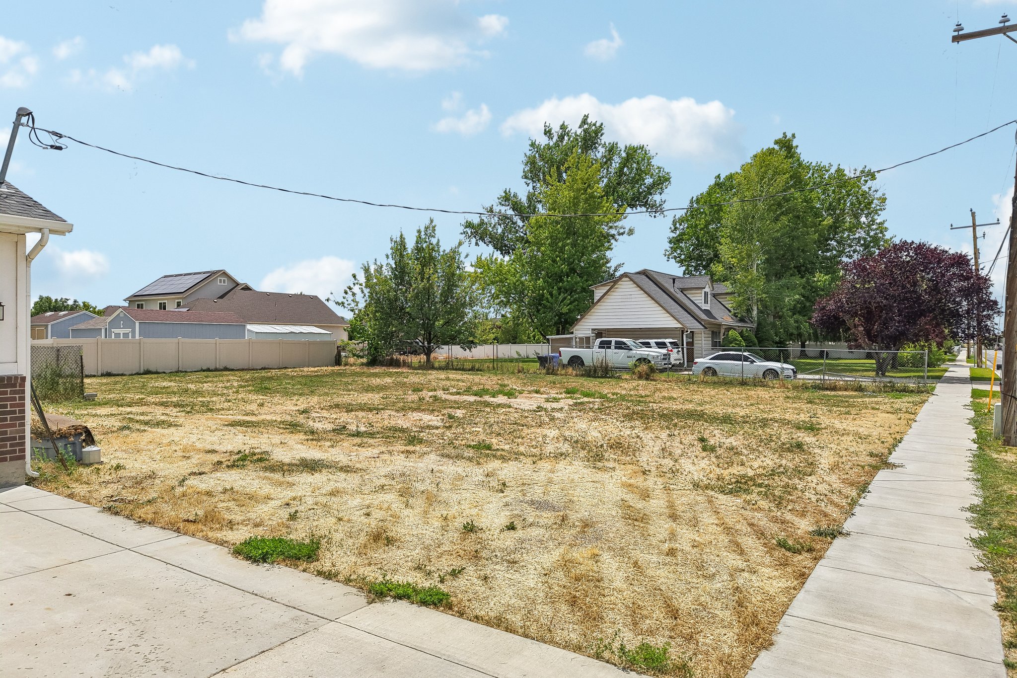 Expansive undeveloped lot featuring street frontage, mature perimeter trees, and a concrete sidewalk border