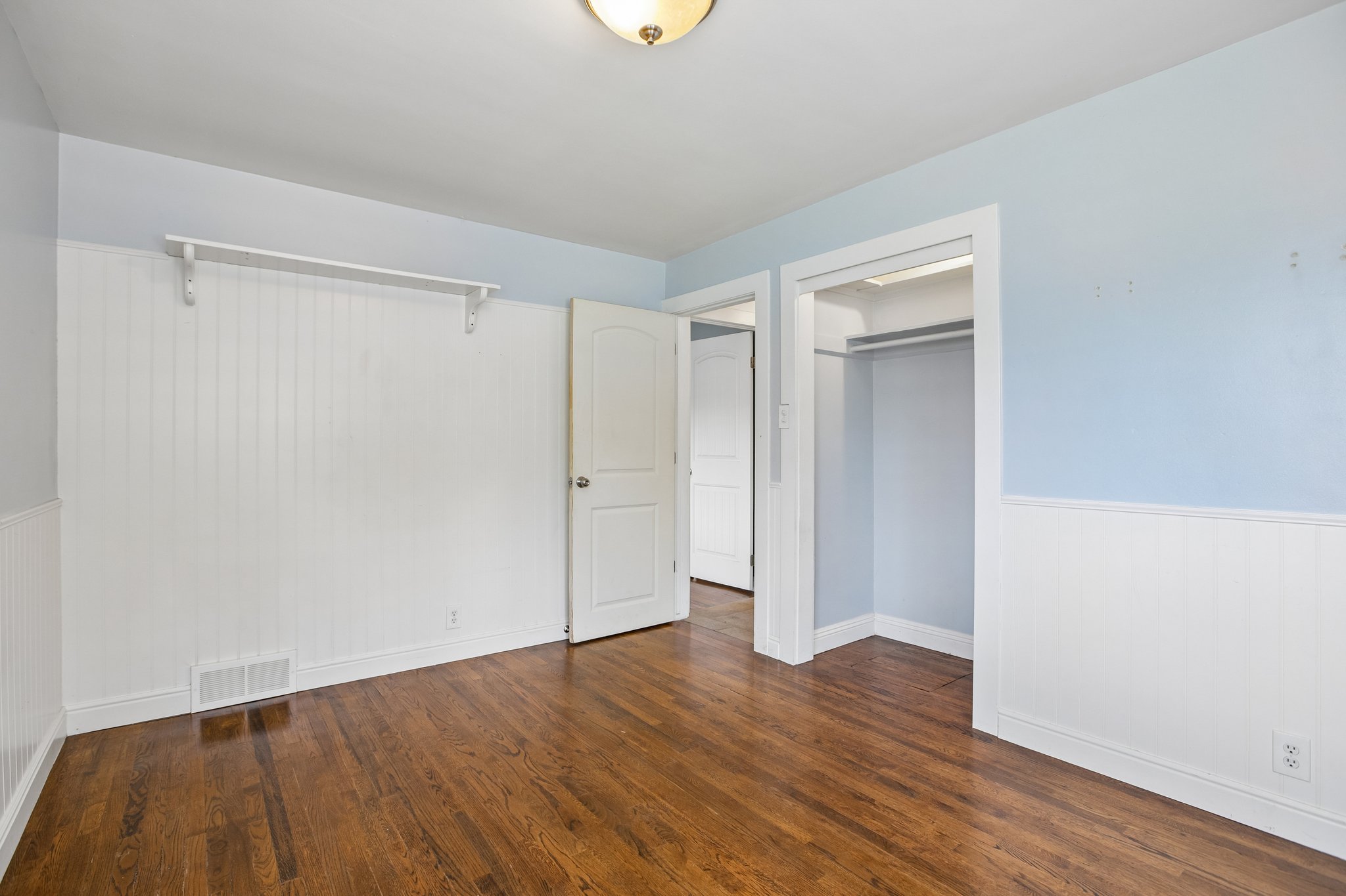 Room featuring rich wood-finish flooring, white wainscoting, and light blue wall paint