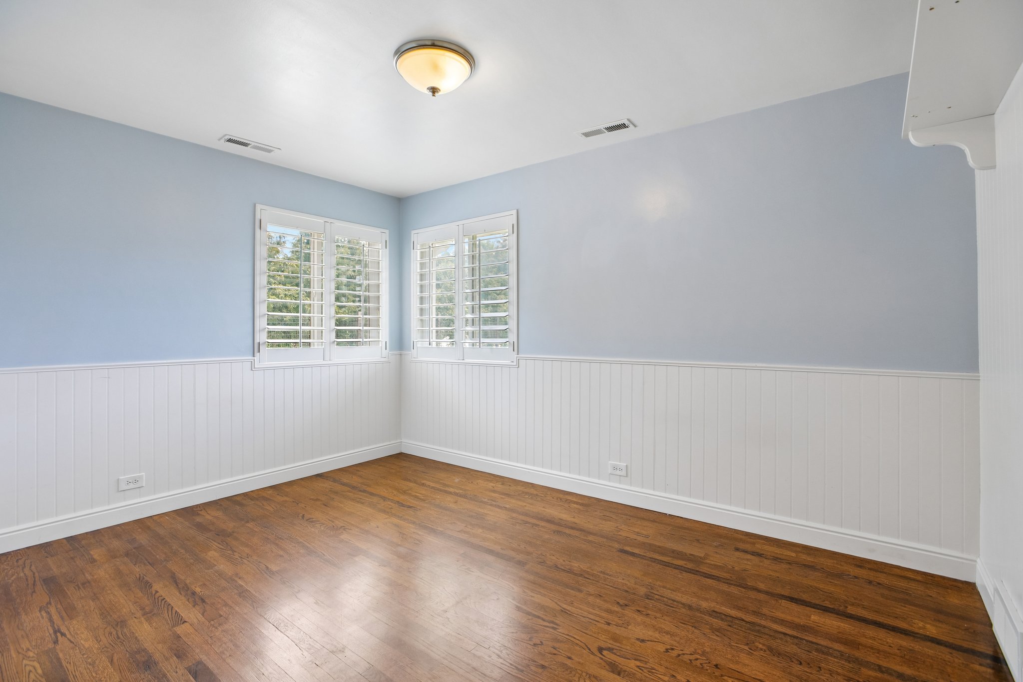 Room featuring wood-finish flooring, white beadboard wainscoting, and light blue walls
