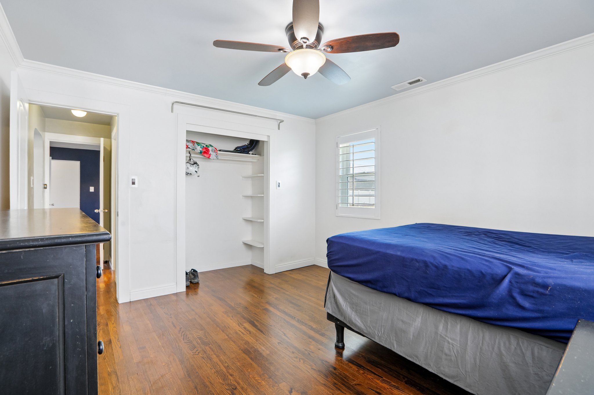 Room with wood-finish flooring, a ceiling fan with integrated lighting, and a window featuring white plantation shutters