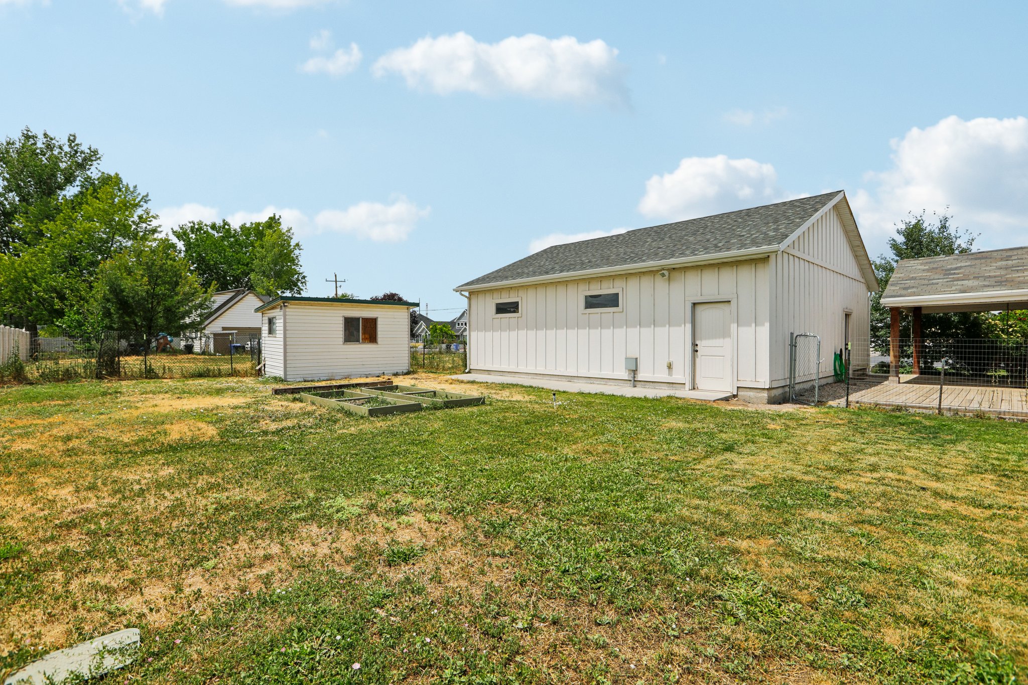 Expansive outdoor space featuring a large detached outbuilding with board and batten siding, a covered patio with a wood deck, a separate storage shed, and a raised garden bed
