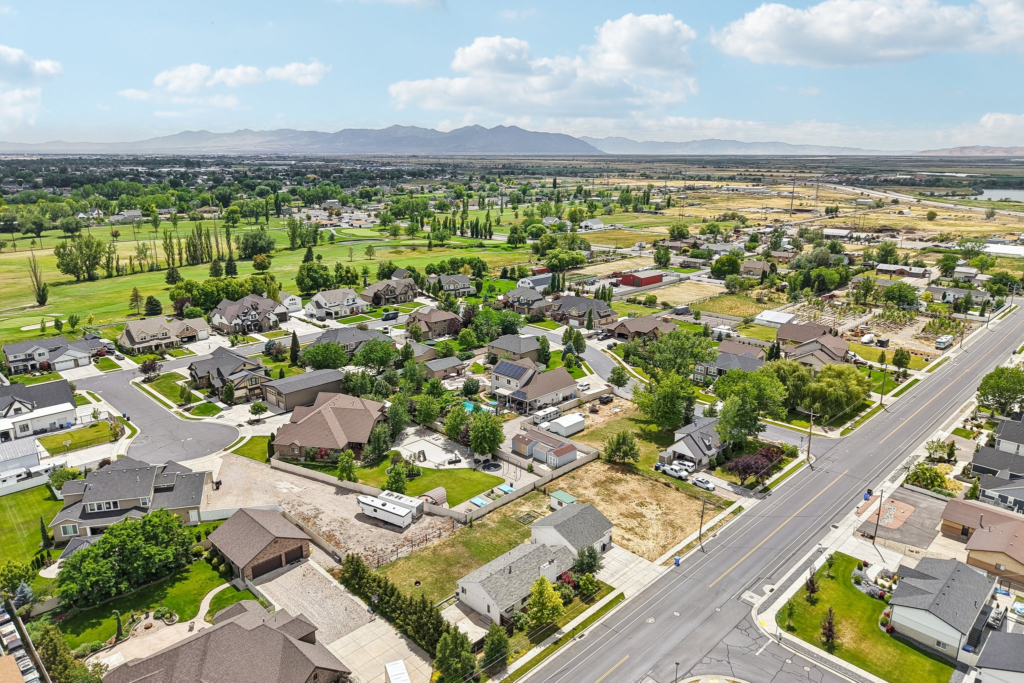 Expansive aerial perspective showcasing a residential neighborhood with surrounding green spaces, a golf course, and distant mountains