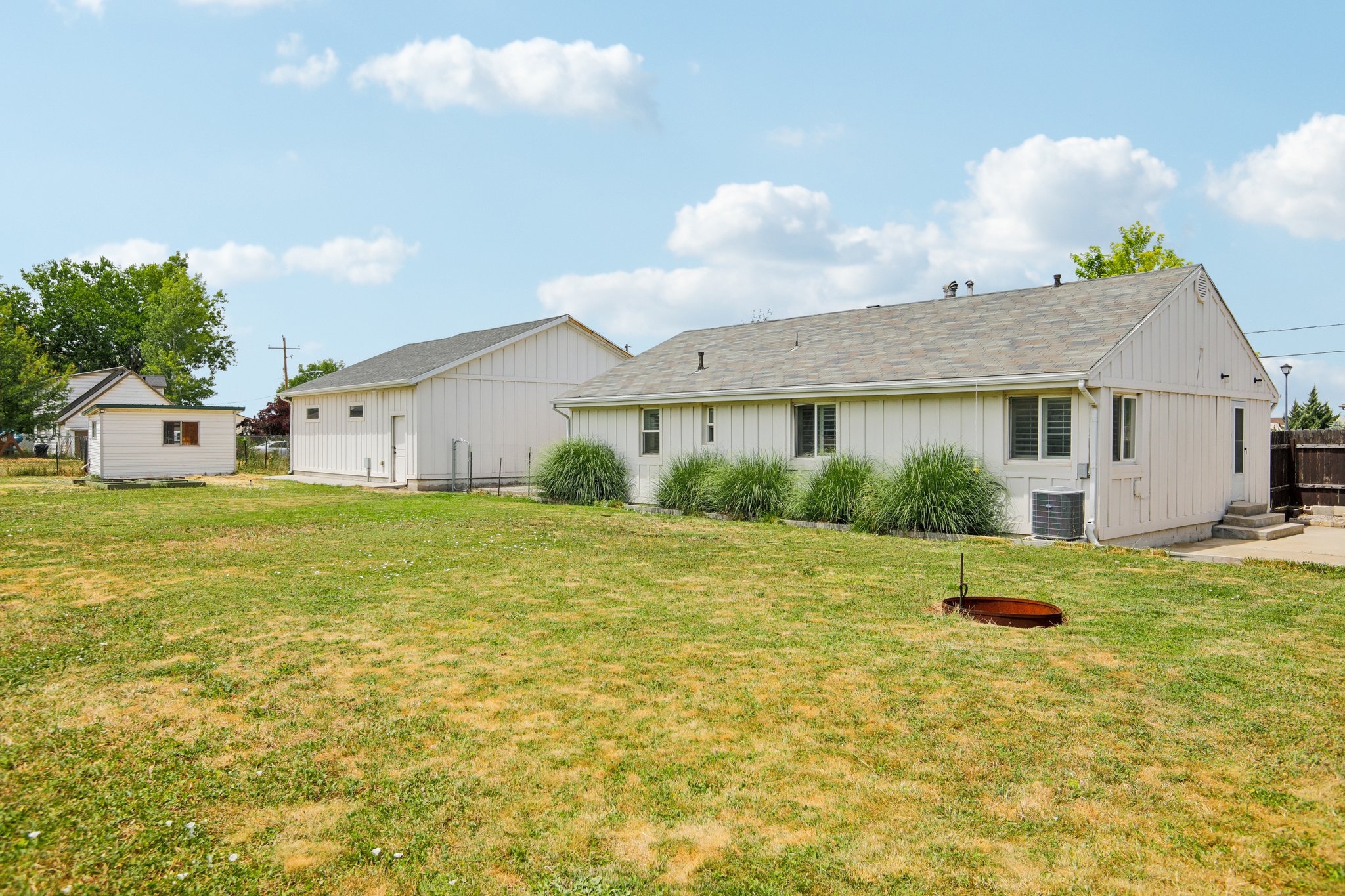 Expansive backyard featuring a detached outbuilding, additional auxiliary structure, and established shrubbery along the main residence