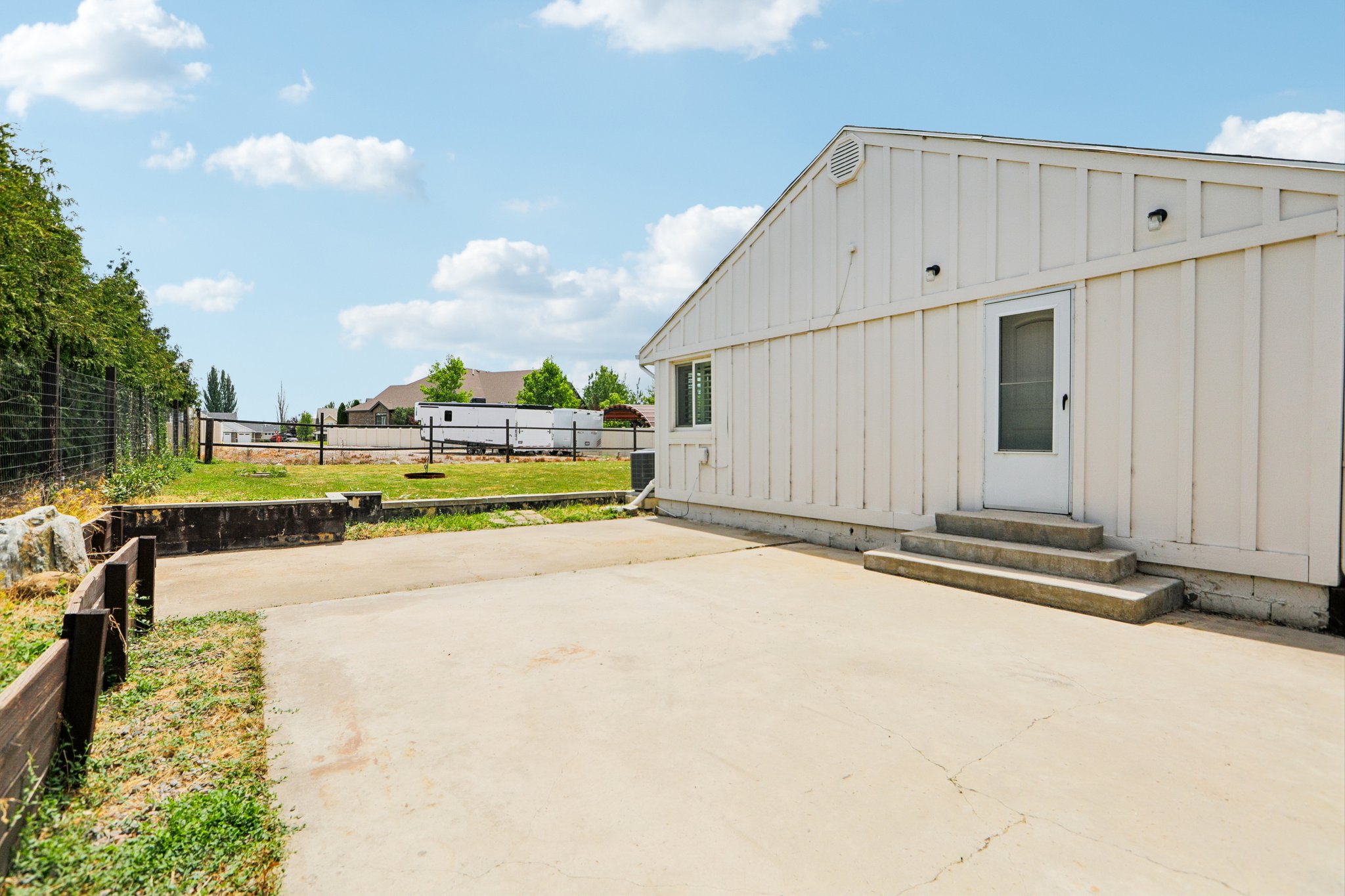 Rear exterior featuring white vertical siding, a white entry door with a screen, and a concrete patio