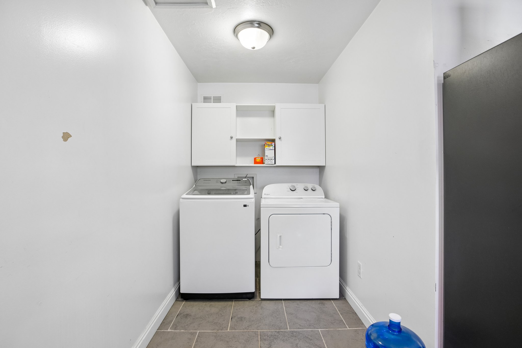 Dedicated laundry area featuring tile flooring, white cabinetry, overhead lighting, and built-in appliances
