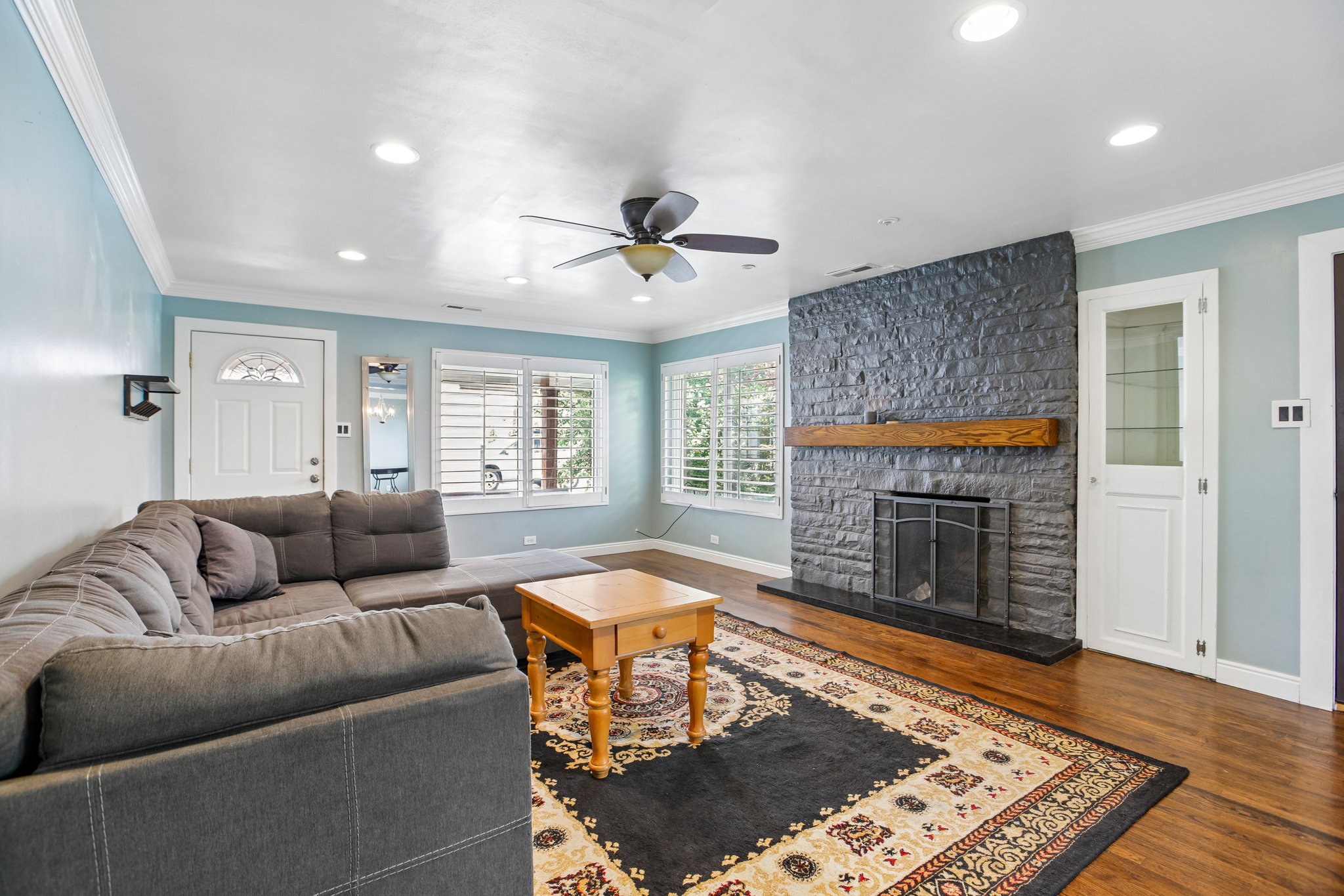 Living area featuring a stone-clad fireplace with a wood mantel, wood-finish flooring, and recessed lighting