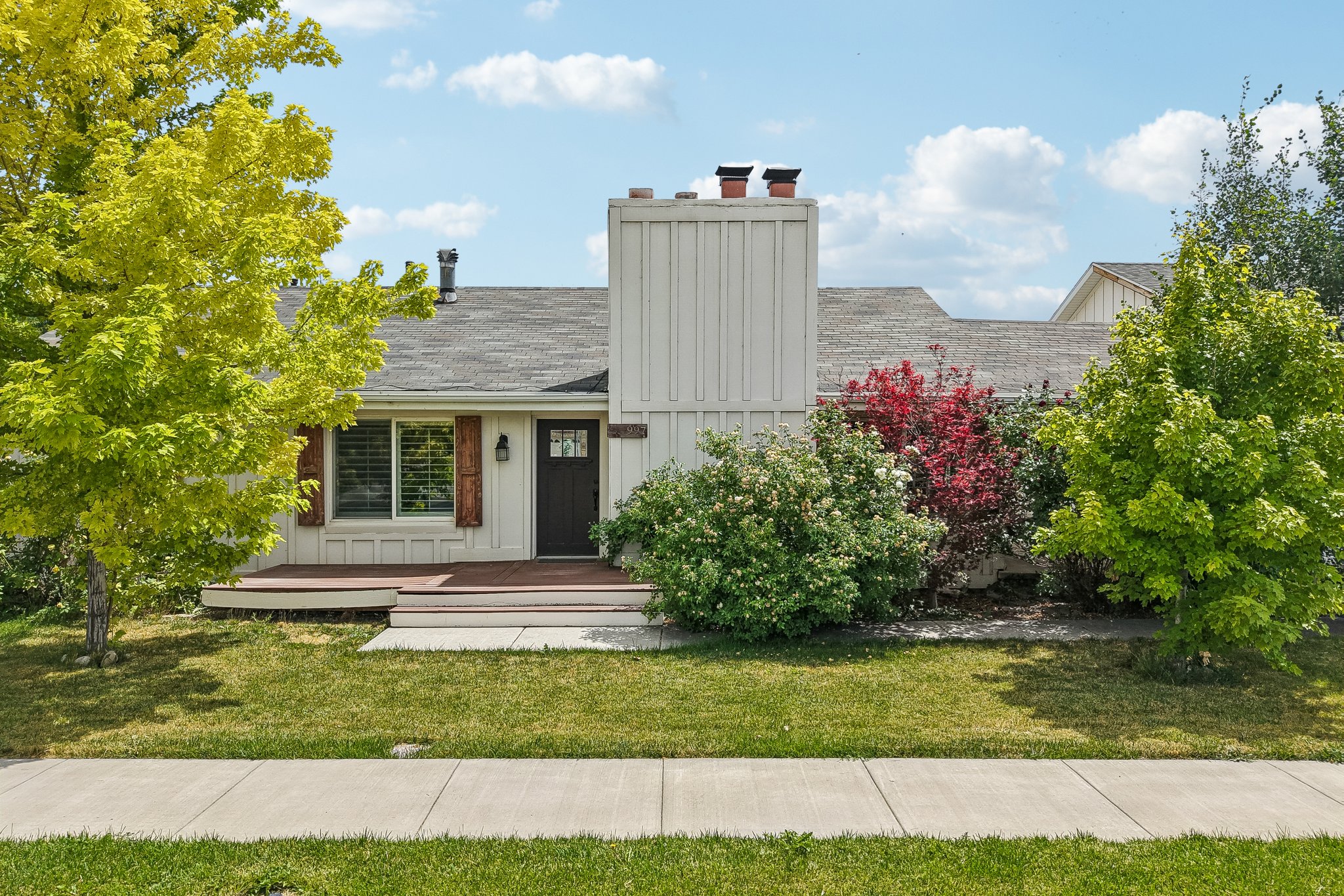 Front exterior featuring a dark wood entry door with glass accents, white siding, and a prominent chimney structure