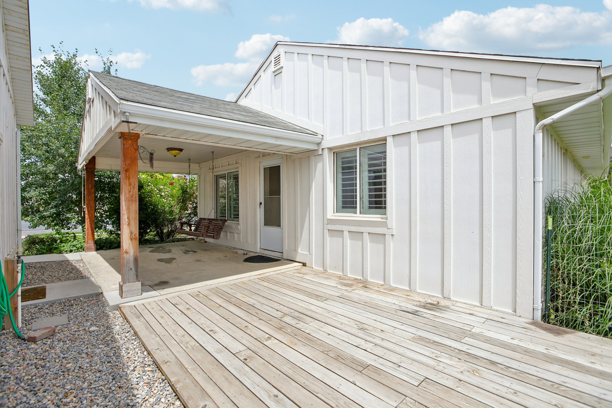 Exterior featuring a covered porch with wooden posts, white board and batten siding, a window with horizontal blinds, and a wooden deck
