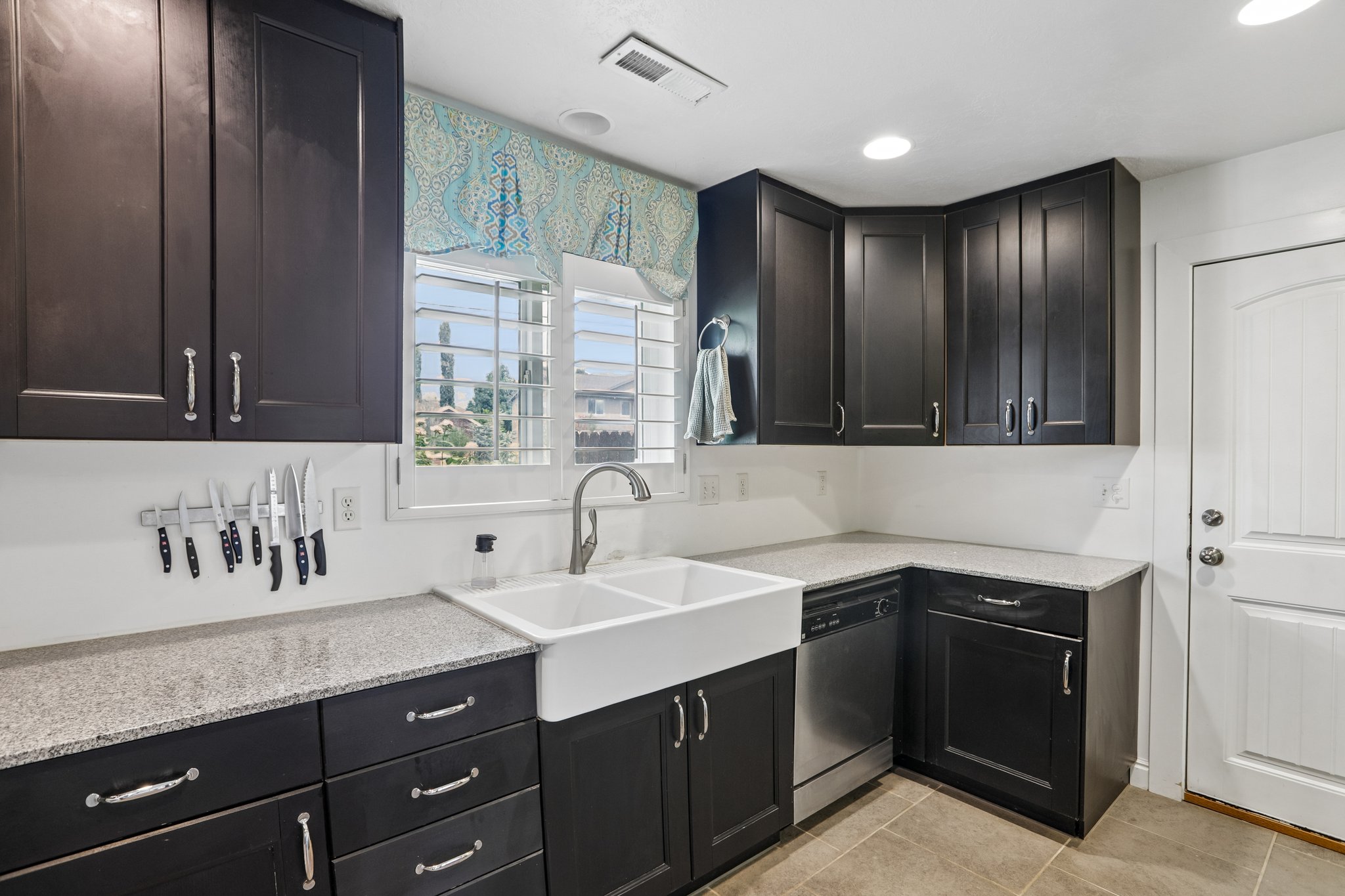 Kitchen featuring dark wood cabinetry, light-toned countertops, a white farmhouse-style double sink, and stainless steel appliances