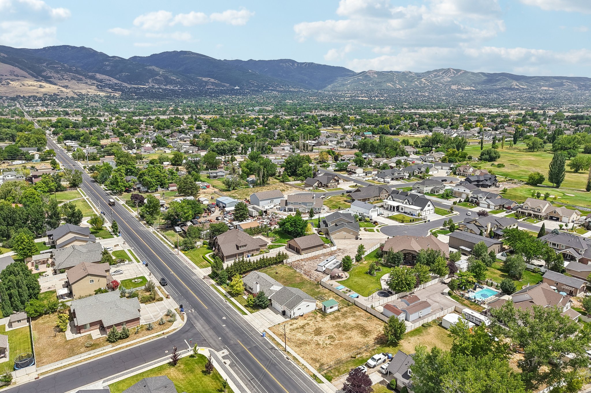 Expansive aerial showcasing a residential neighborhood with varied architectural styles, mature landscaping, and mountainous terrain in the background