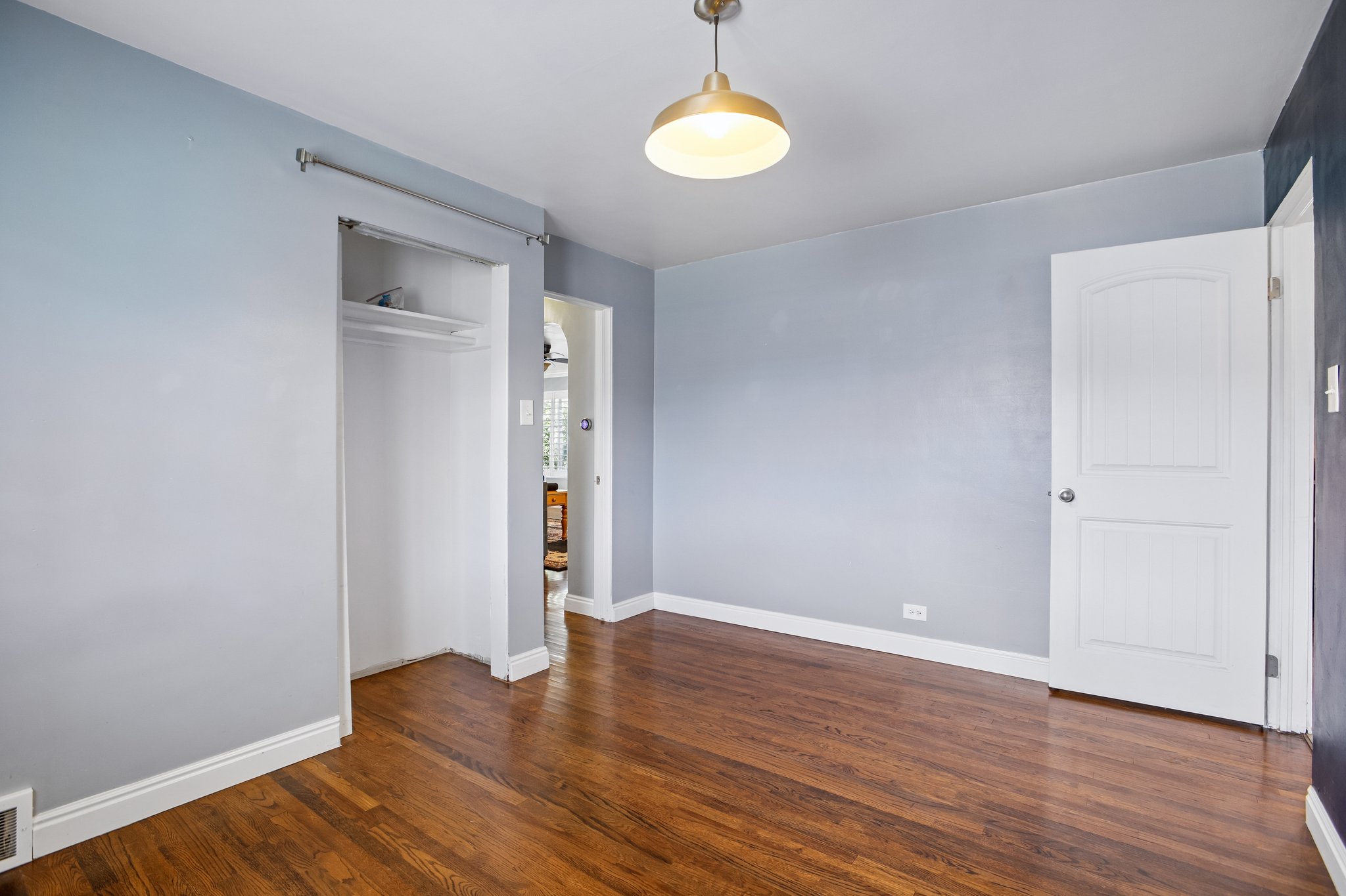 Room featuring wood-finish flooring, light blue wall paint, a built-in closet with shelving, and a white paneled interior door