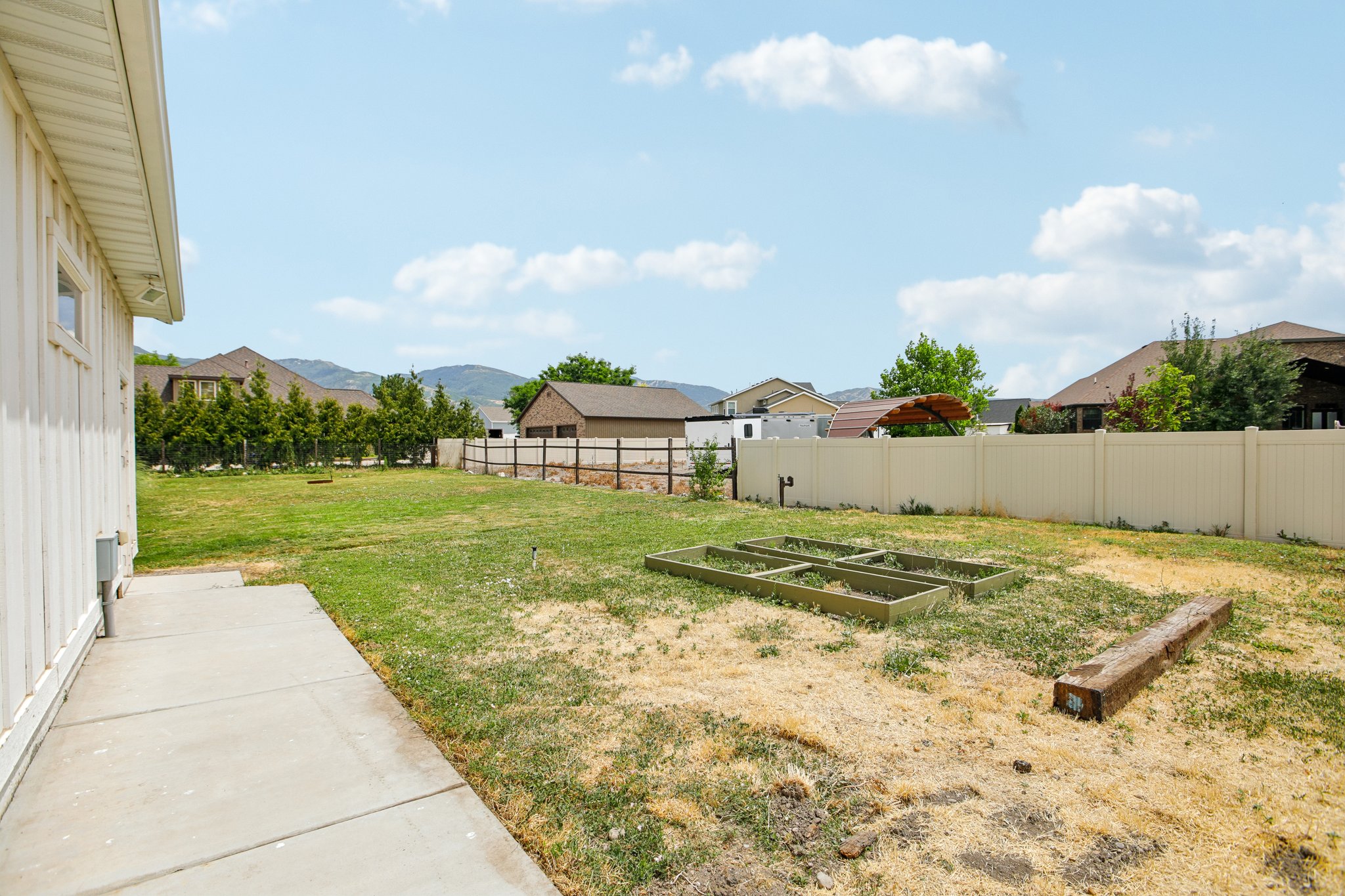 Expansive backyard featuring a concrete patio, board and batten siding, wooden planter boxes, and a privacy fence