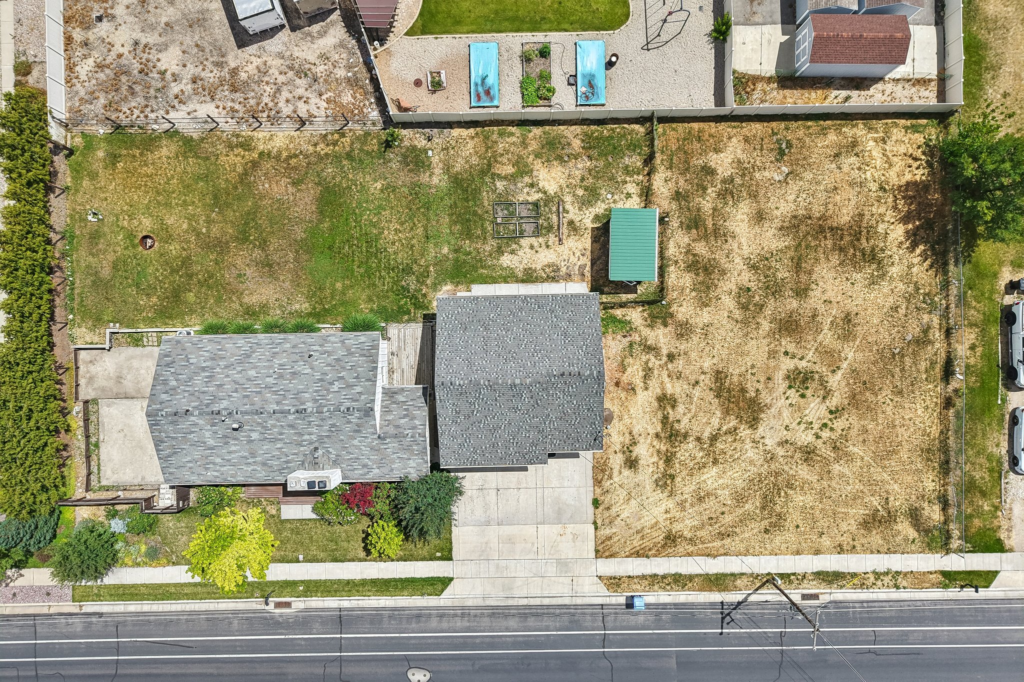 Aerial perspective showcasing two distinct structures with gray shingle roofing and a prominent concrete driveway
