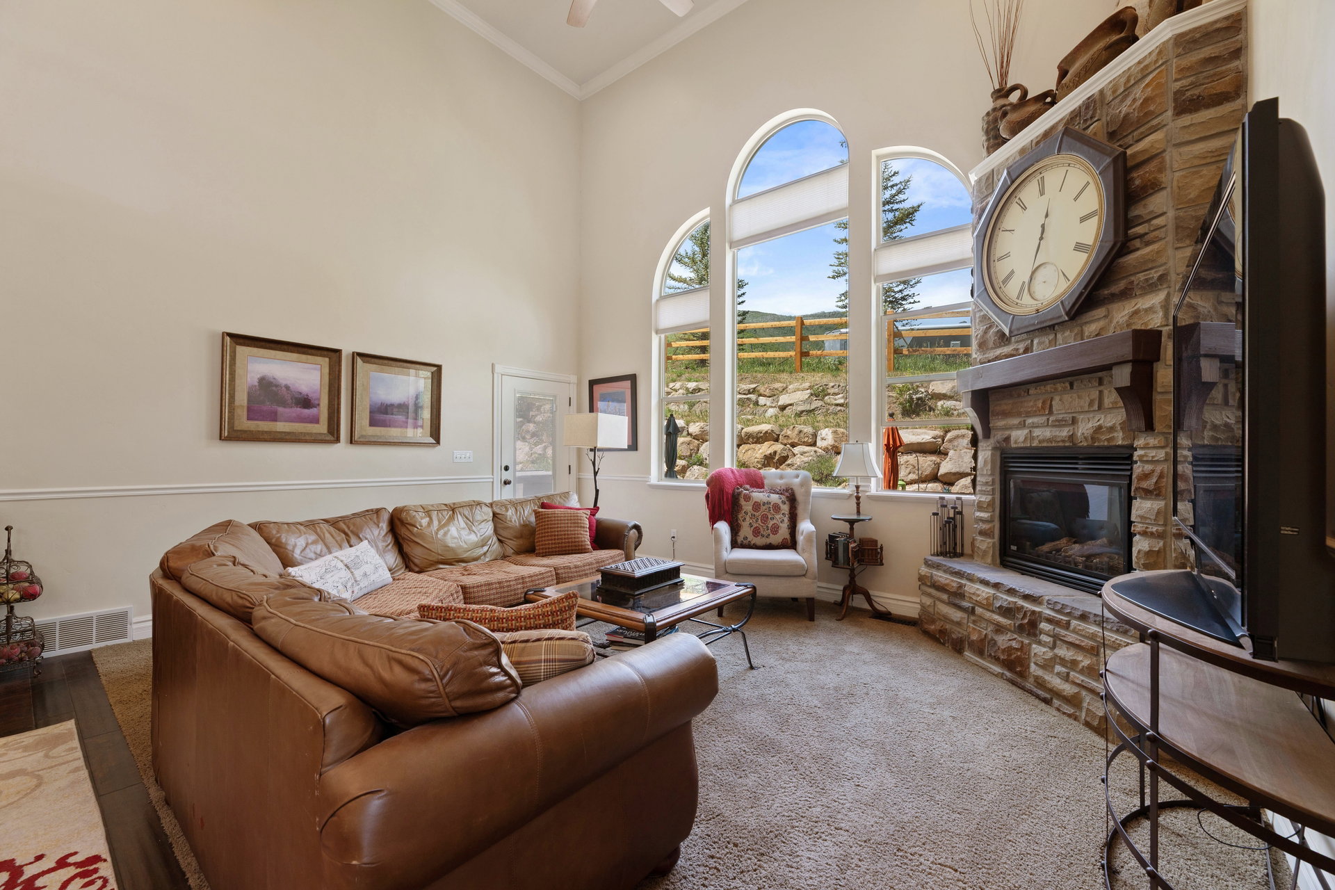 Living area featuring a stone-clad fireplace with a wood mantel, arched windows, light tan wall color, and high ceilings