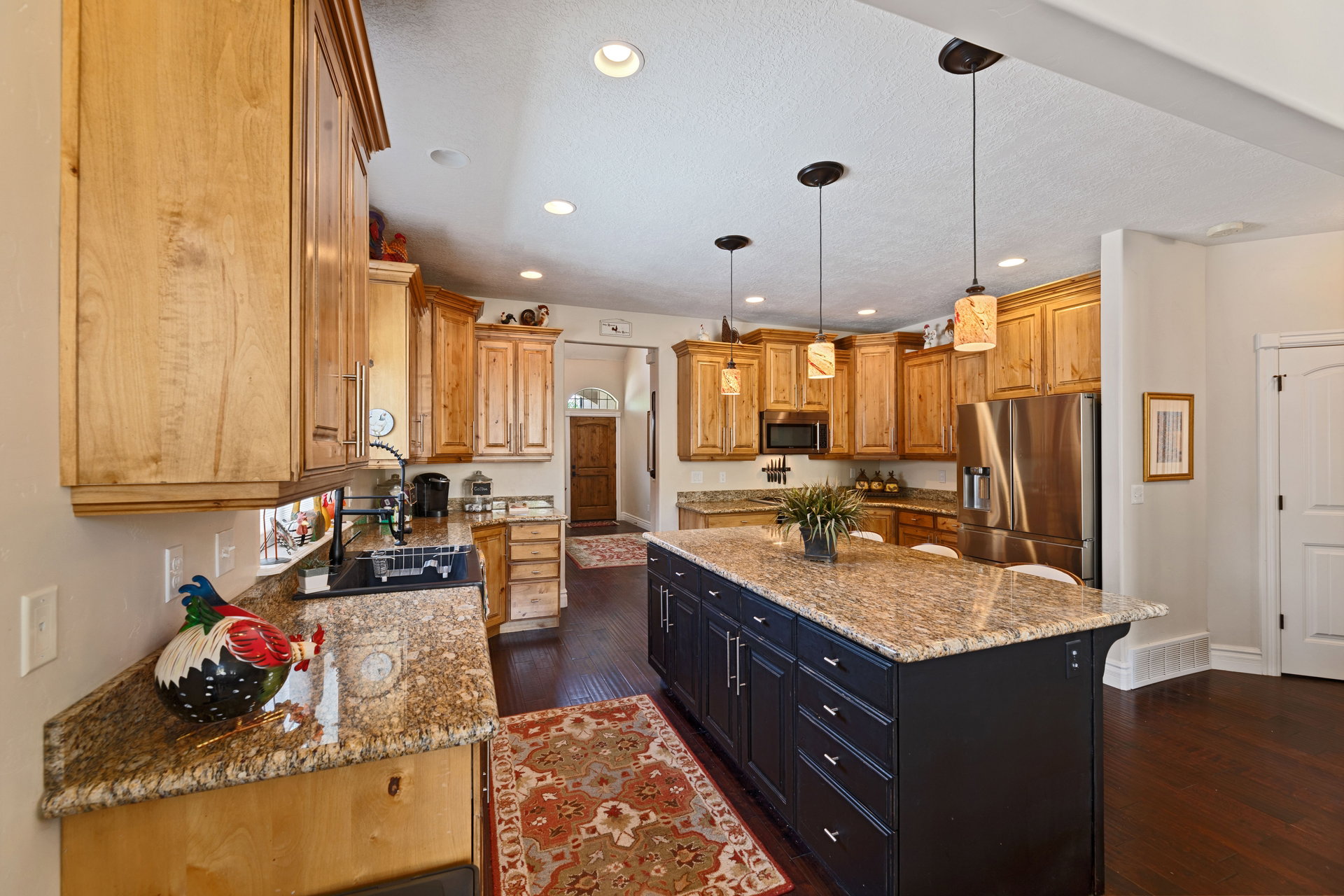 Spacious kitchen featuring an expansive center island with counter seating, light-toned wood cabinetry, dark wood-finish flooring, recessed lighting, and stainless steel appliances
