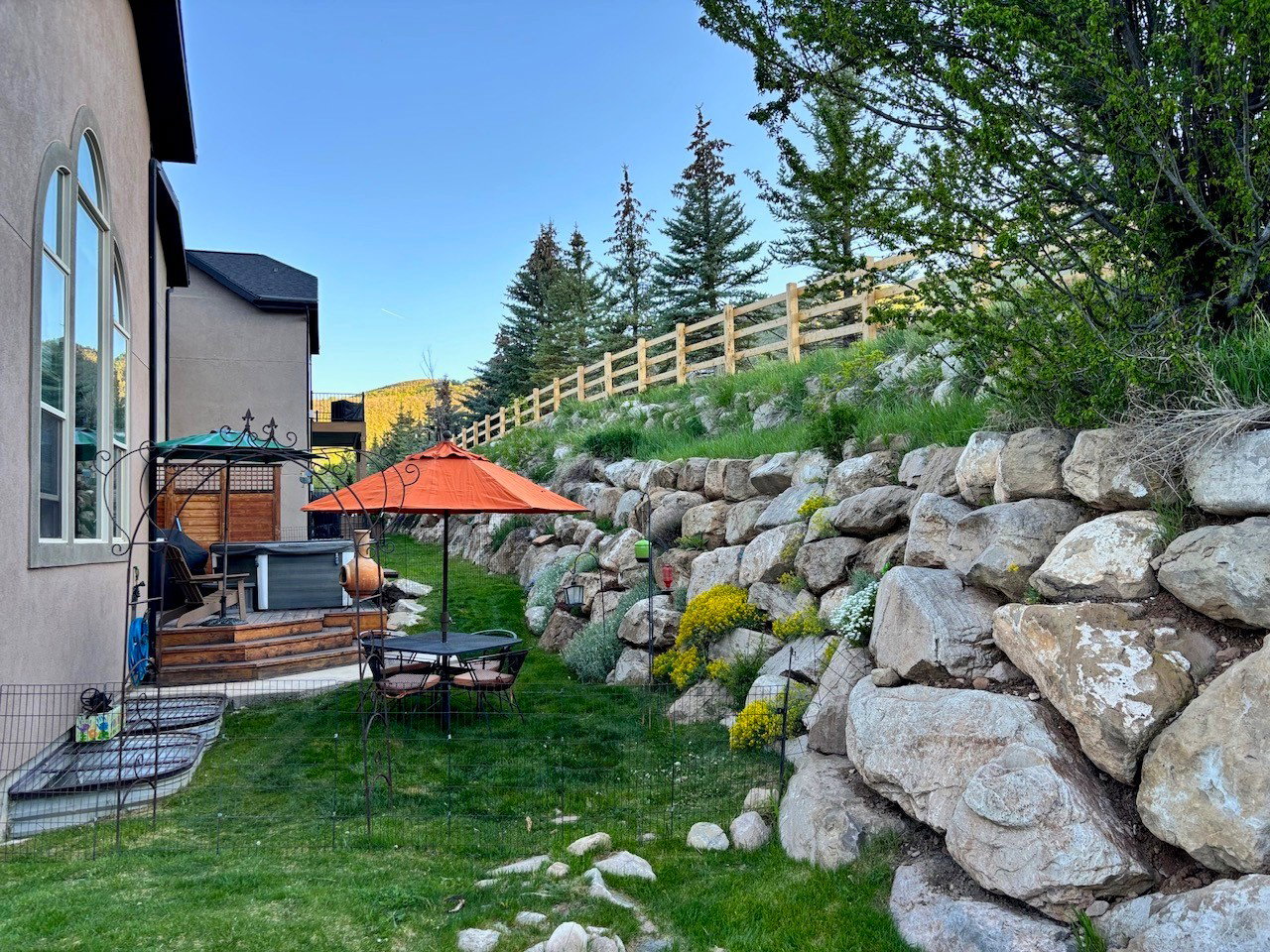 Tiered backyard featuring a rock retaining wall with established plantings, a wooden deck