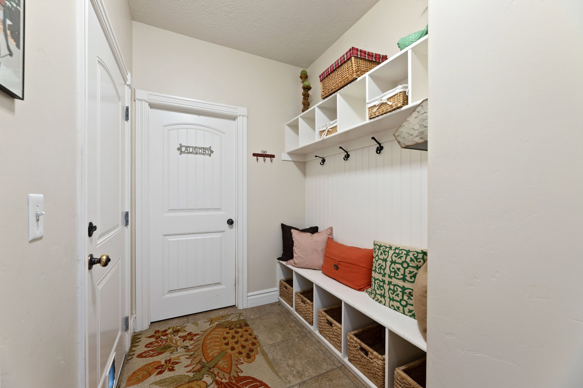 Hallway entry featuring tile flooring, white built-in storage bench, white beadboard wall paneling, and white overhead shelving