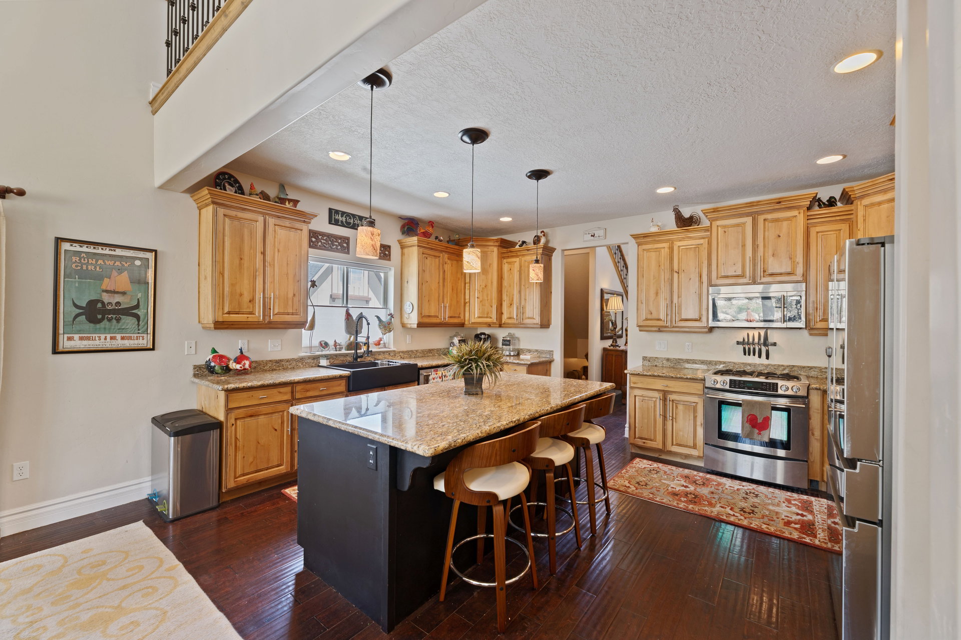 Spacious kitchen featuring rich wood-finish flooring, light wood cabinetry, granite countertops, and stainless steel appliances