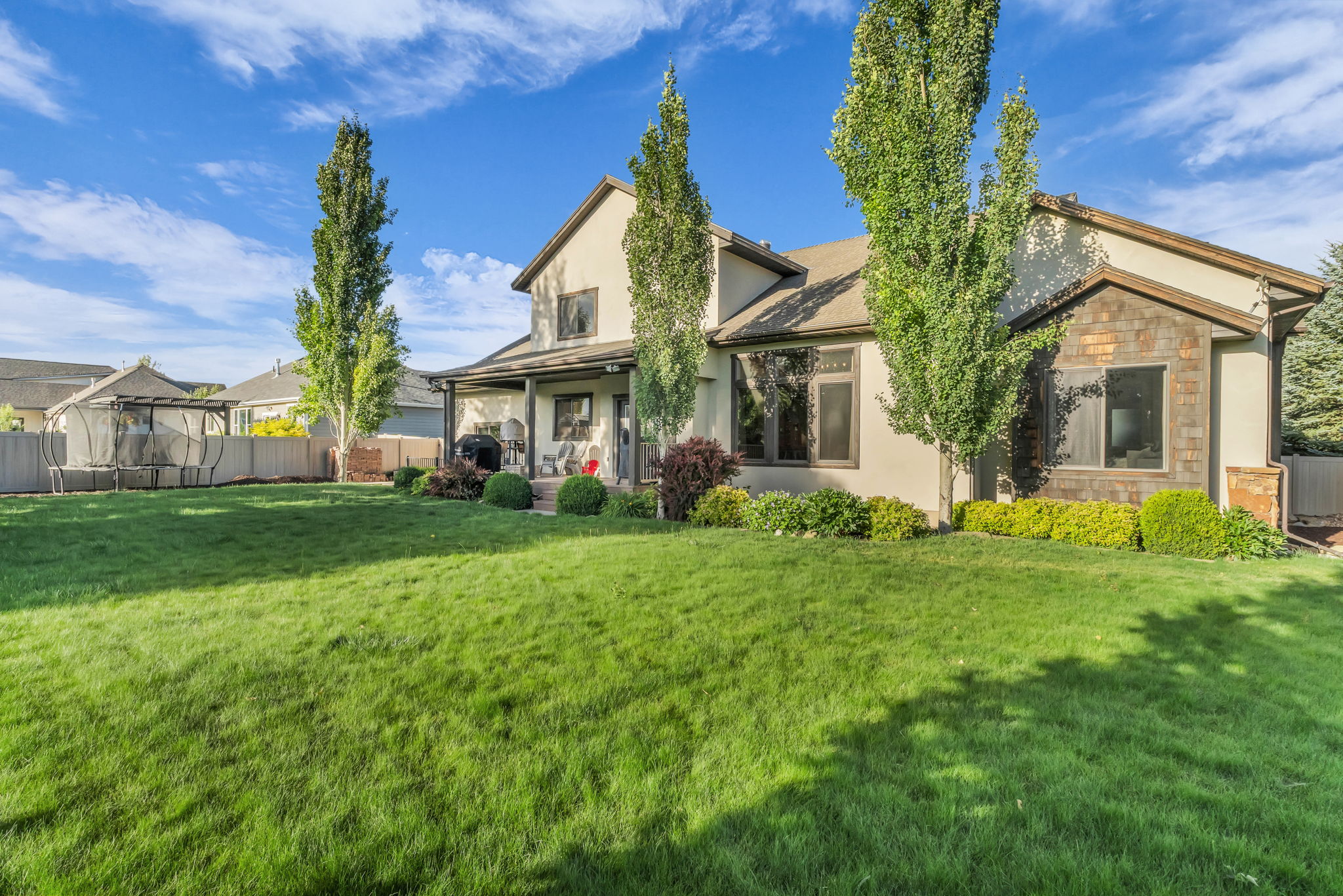 Expansive rear yard with a manicured lawn, established landscaping, and mature trees