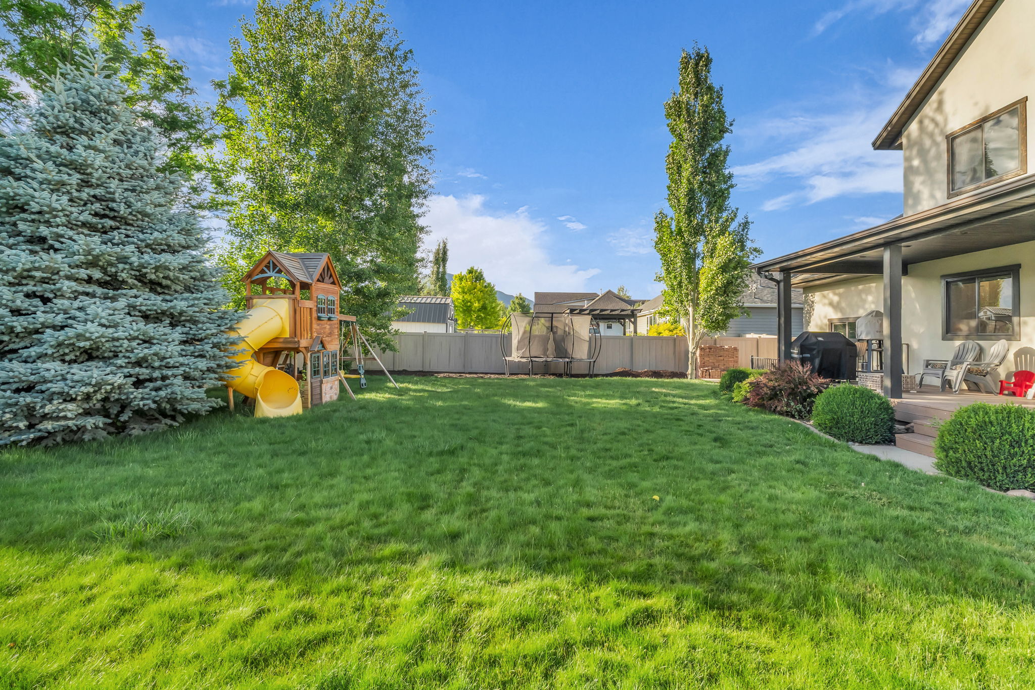 Expansive green lawn with mature trees and a covered patio area