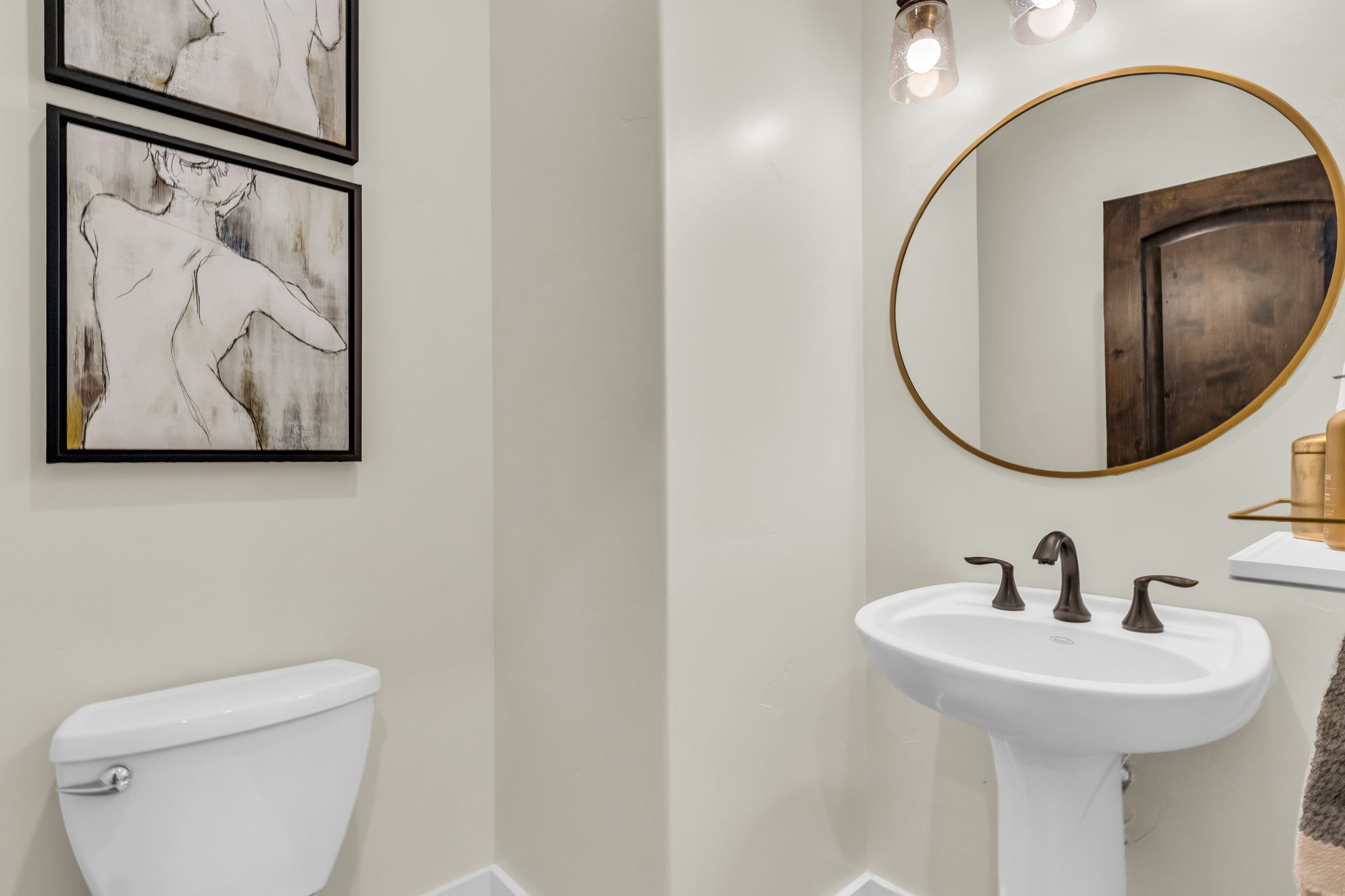 Pedestal sink with oil-rubbed bronze faucet fixtures, round gold-framed mirror, and contemporary vanity lighting
