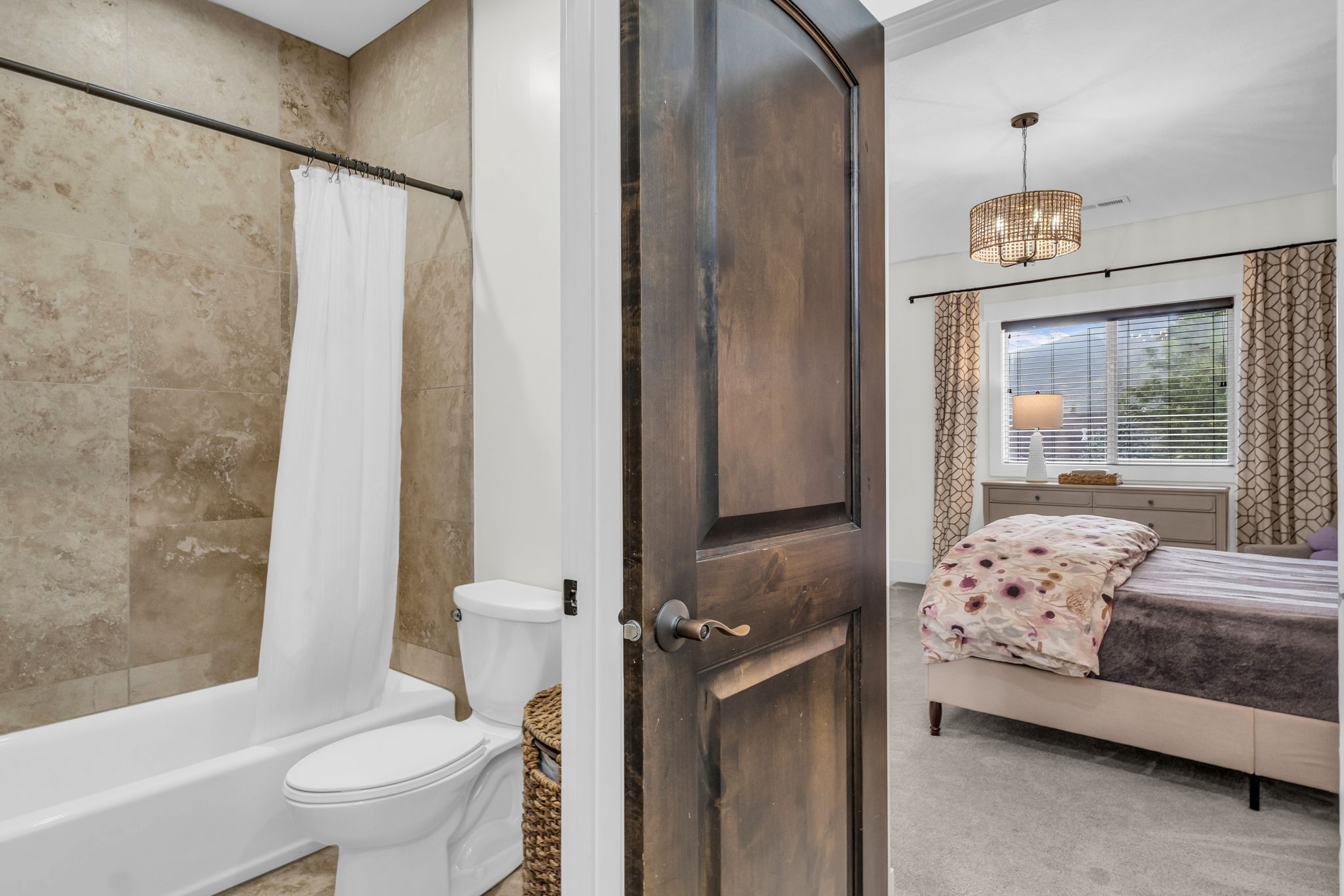 Bathroom featuring a full-size tub with a shower, floor-to-ceiling tile surround, and a white toilet