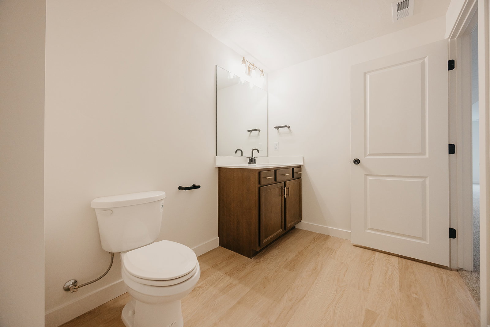 Bathroom featuring a wood-finish vanity with a light-toned countertop, a rectangular mirror, and matte black fixtures