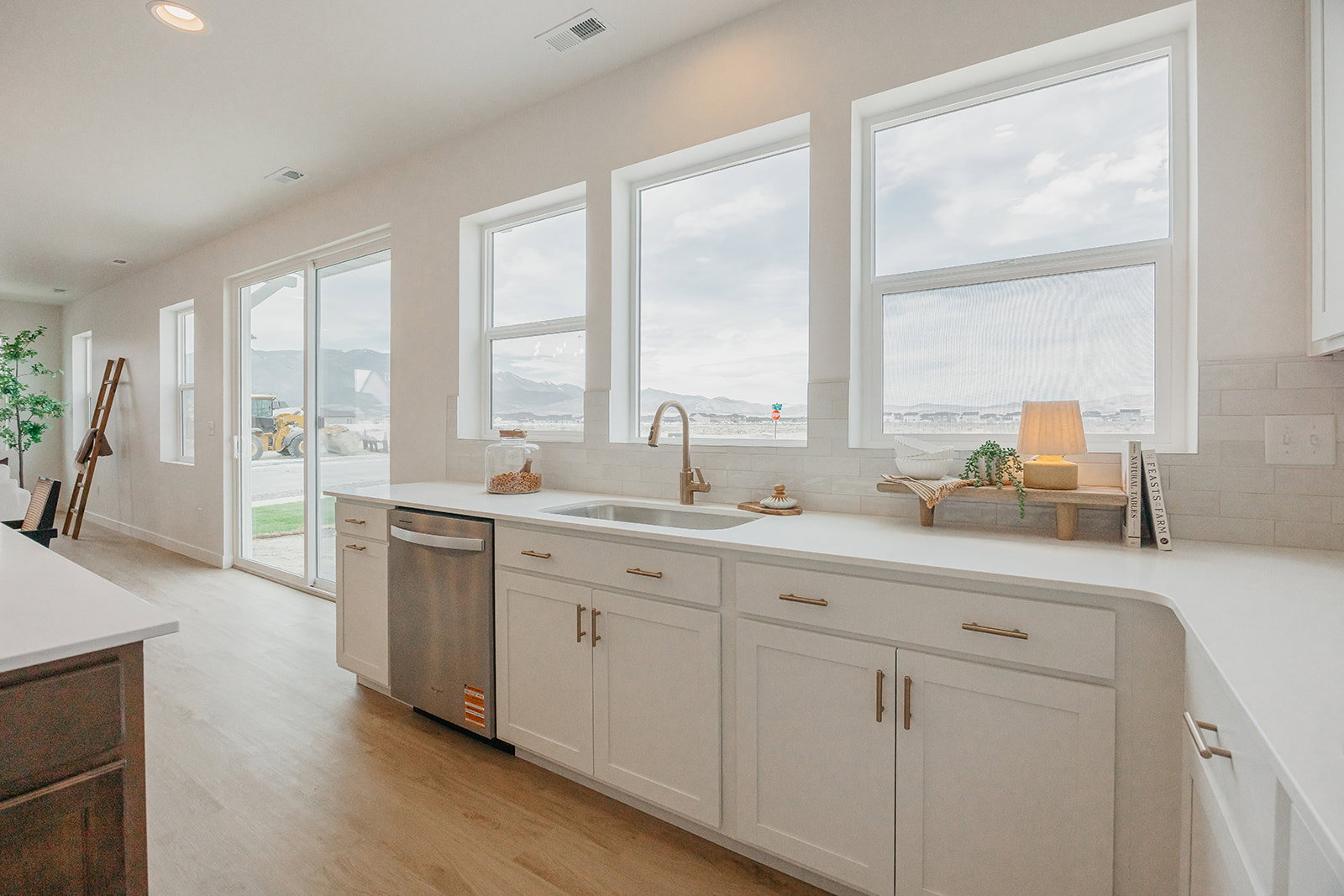 Kitchen featuring a stainless steel dishwasher, undermount sink with a brass-finish faucet, and white shaker-style cabinetry with brass-finish hardware