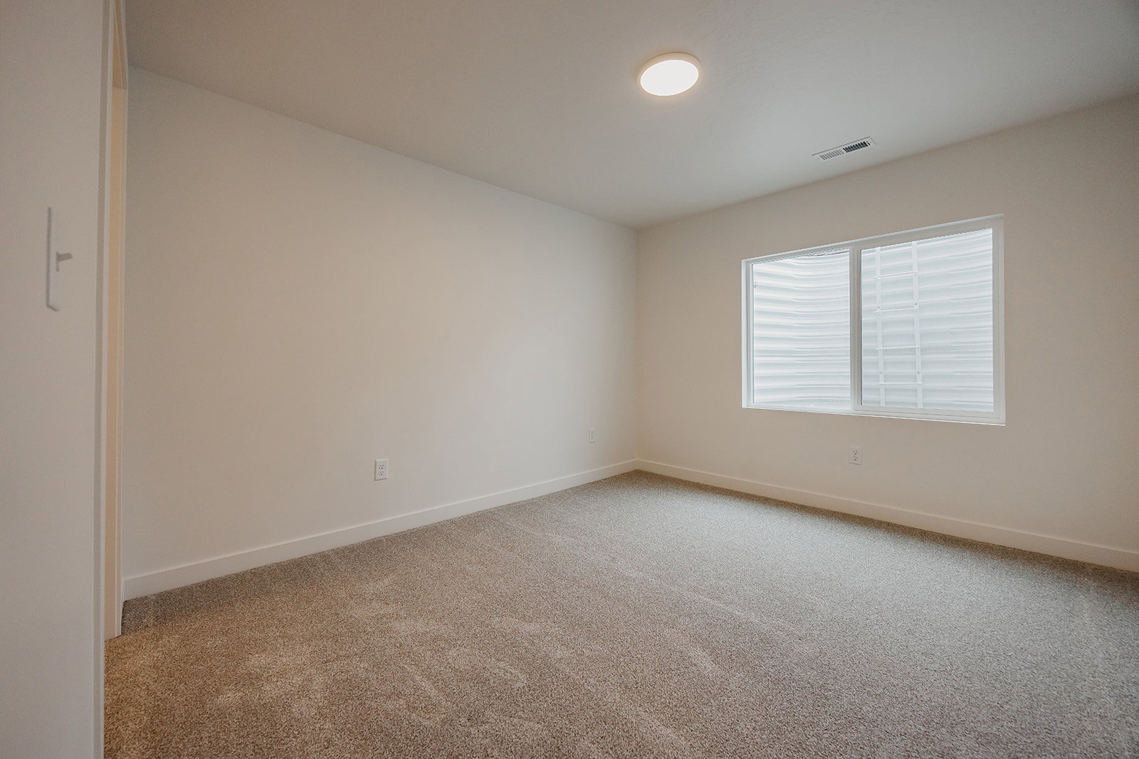 Spacious room featuring neutral carpeting, light-colored walls, and a large window with horizontal blinds