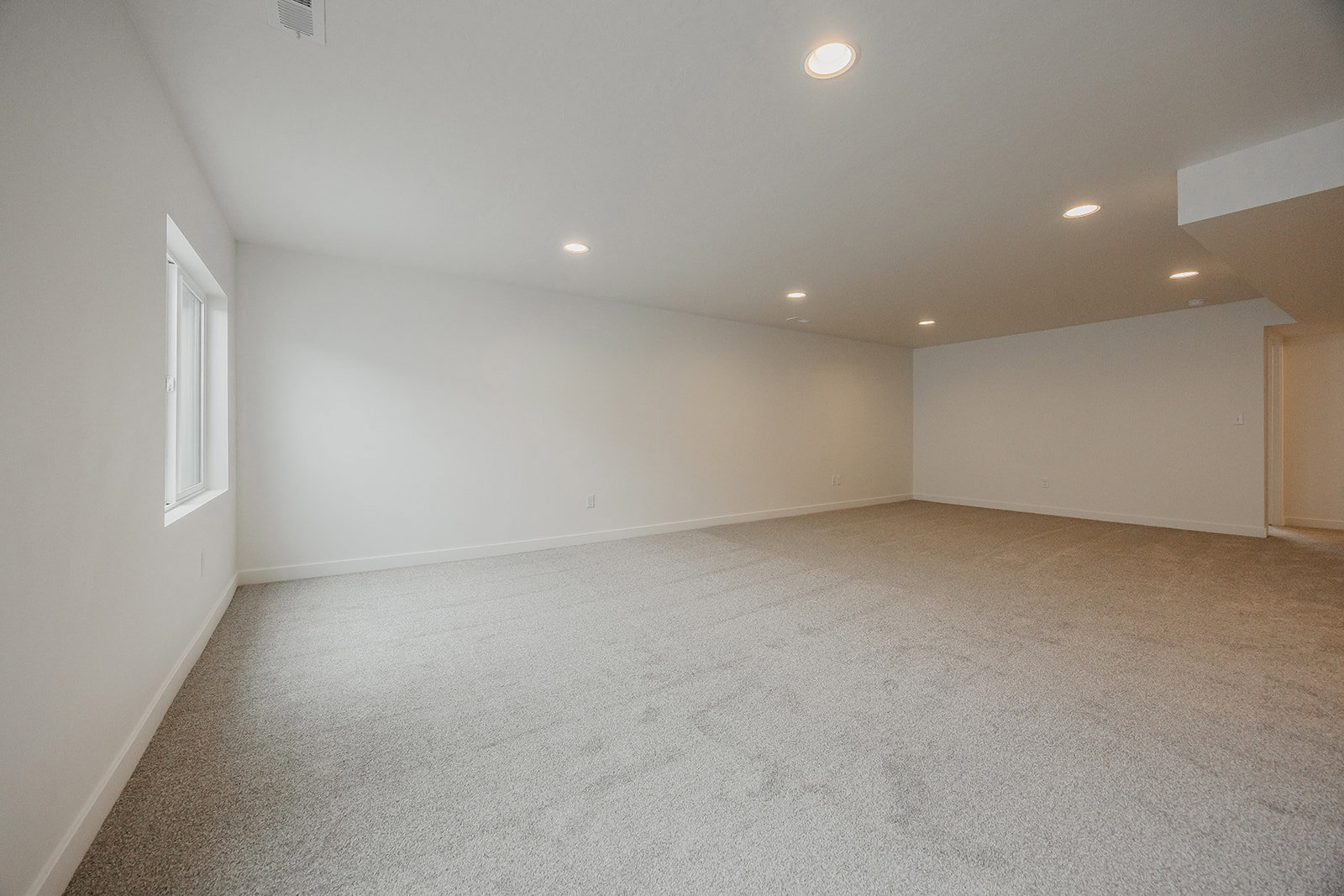 Spacious lower-level room featuring light gray carpeting, neutral wall finishes, recessed lighting, a single window, and white trim