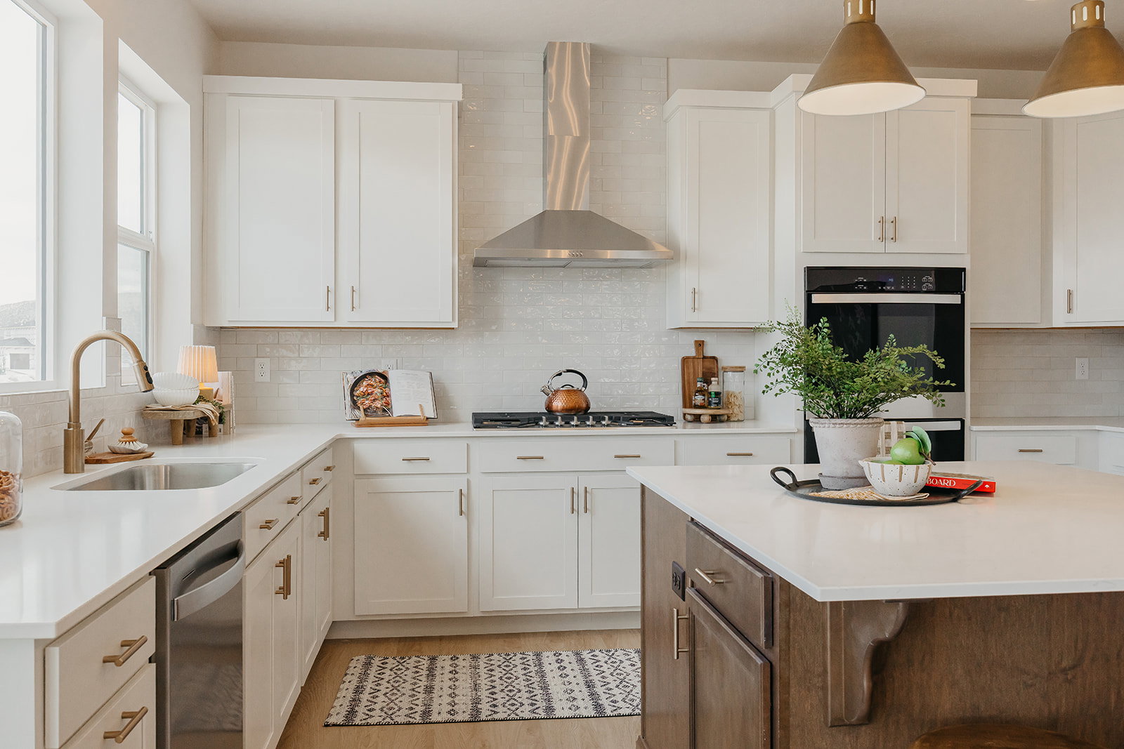Modern kitchen showcasing white cabinetry, a stainless steel range hood, built-in double ovens, and a central island with a contrasting wood-finish base