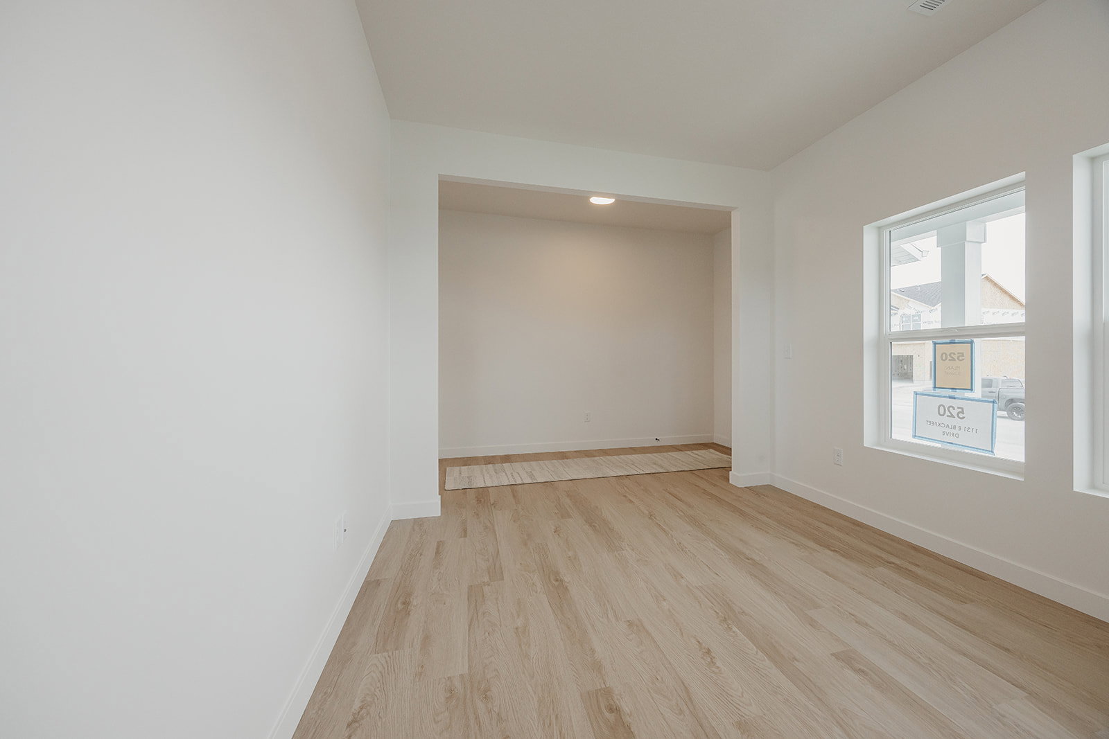 Spacious room featuring light wood-finish flooring, white walls, and bright window fixtures