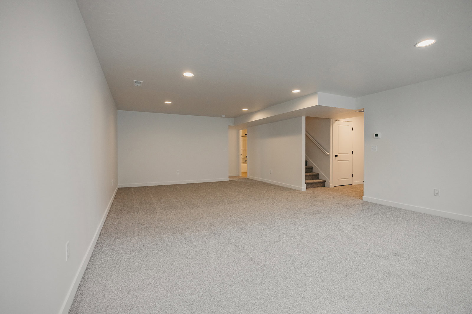 Spacious room featuring neutral carpet flooring, recessed lighting, white walls, and a white interior door
