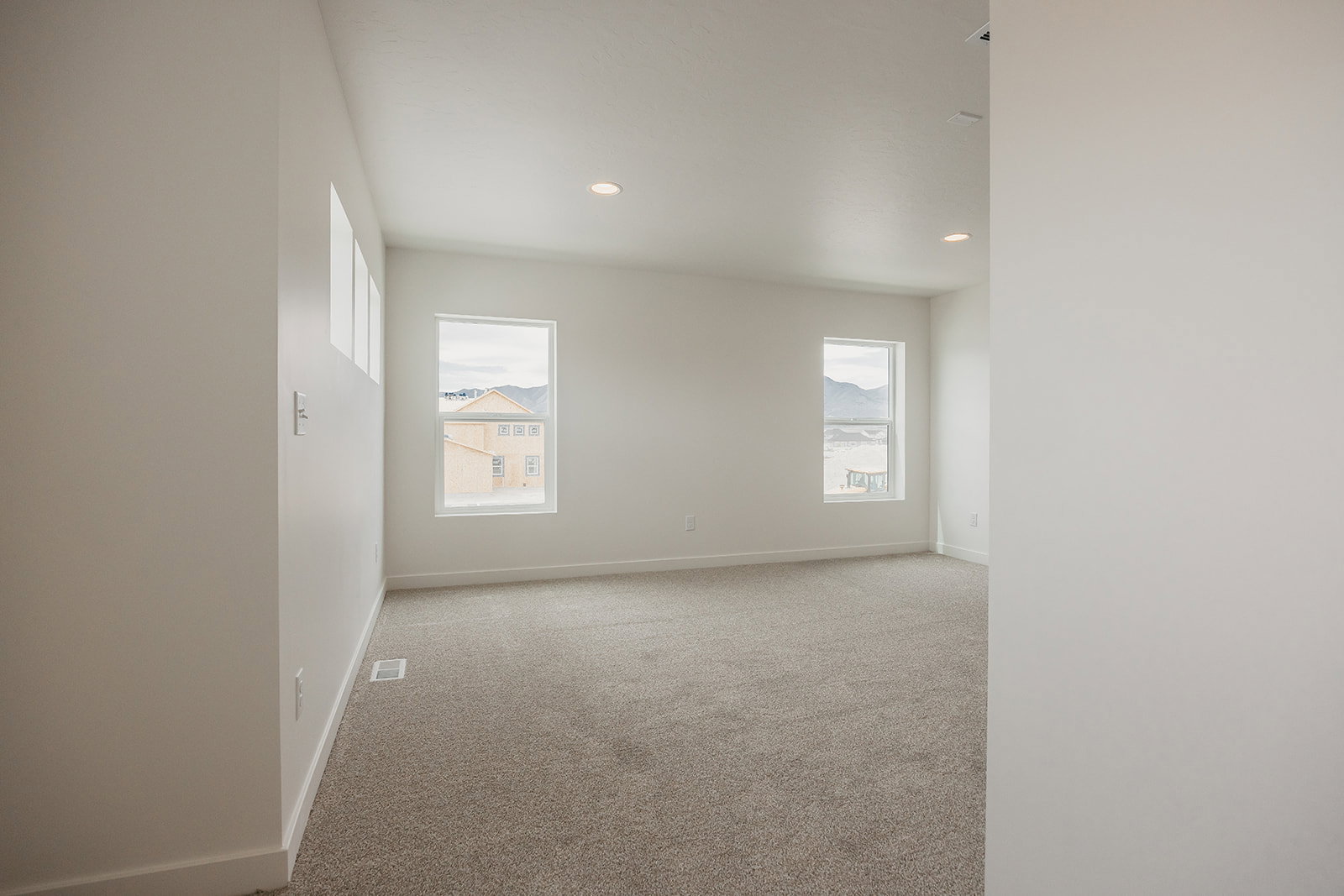 Spacious interior room featuring light-colored carpeting, multiple windows, and recessed ceiling lighting