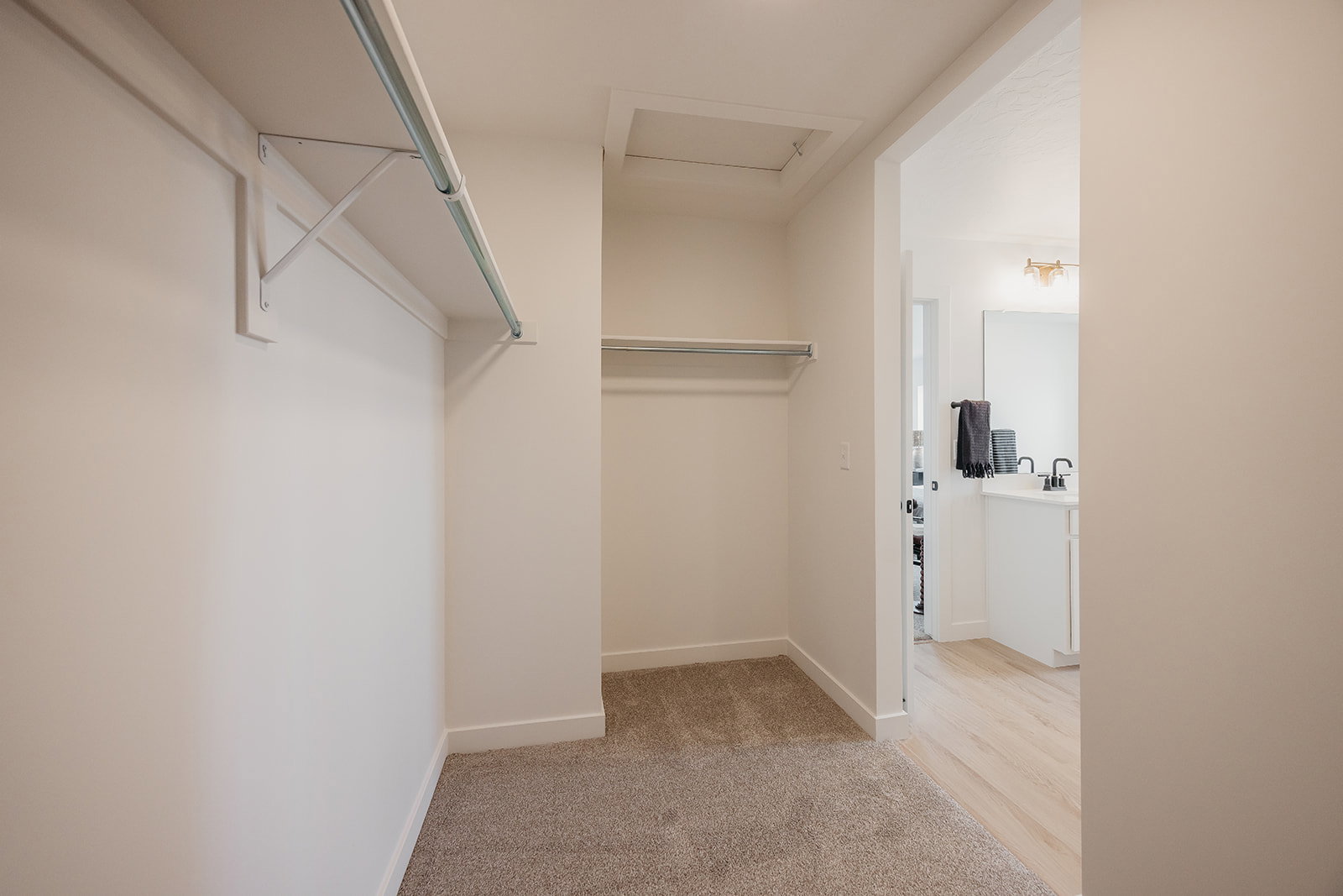 Walk-in closet featuring carpet flooring, two clothing rods, and an access panel