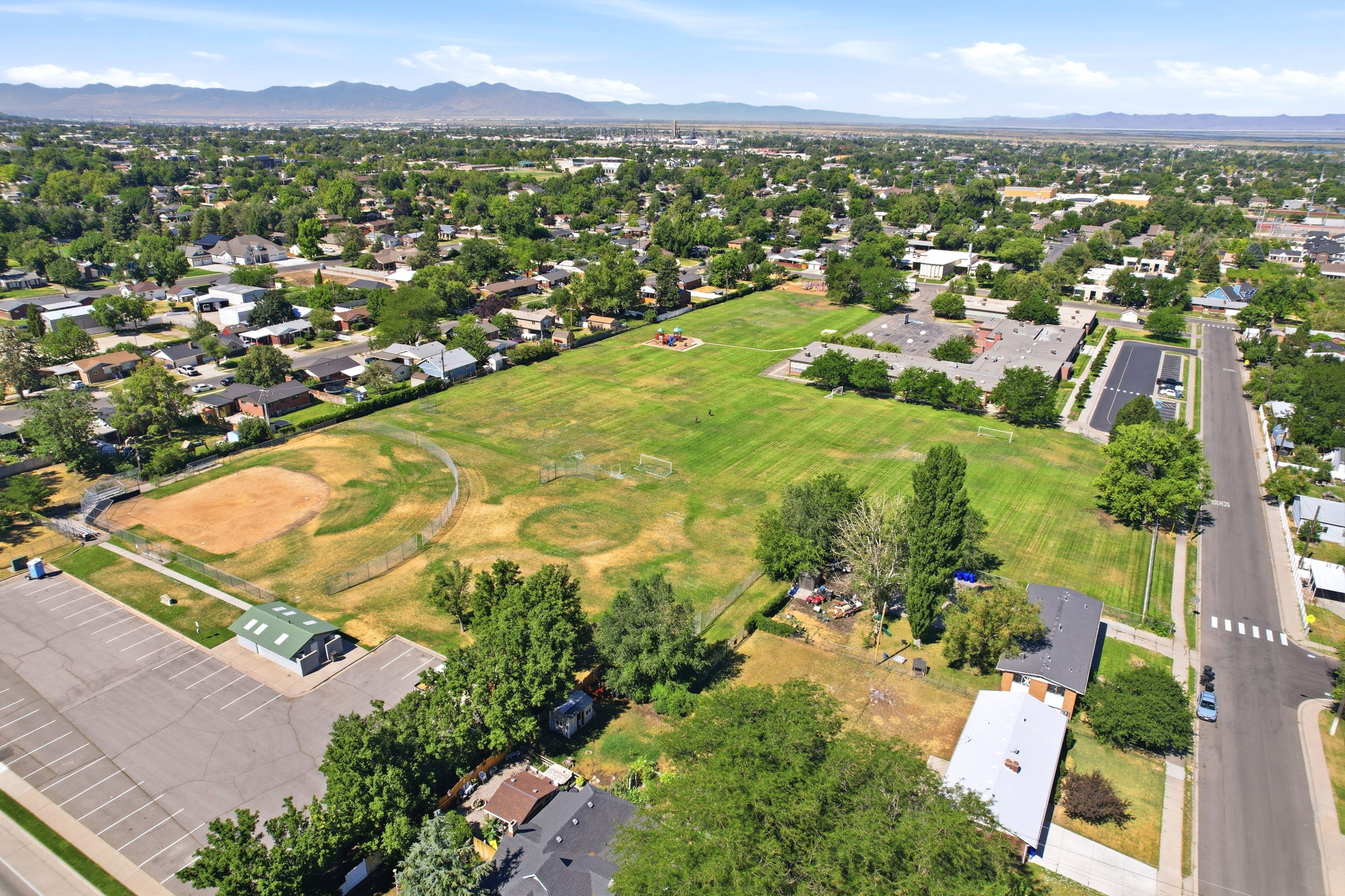 Expansive green space bordered by residential homes, featuring a baseball diamond, additional sports fields, and a nearby building with a parking area