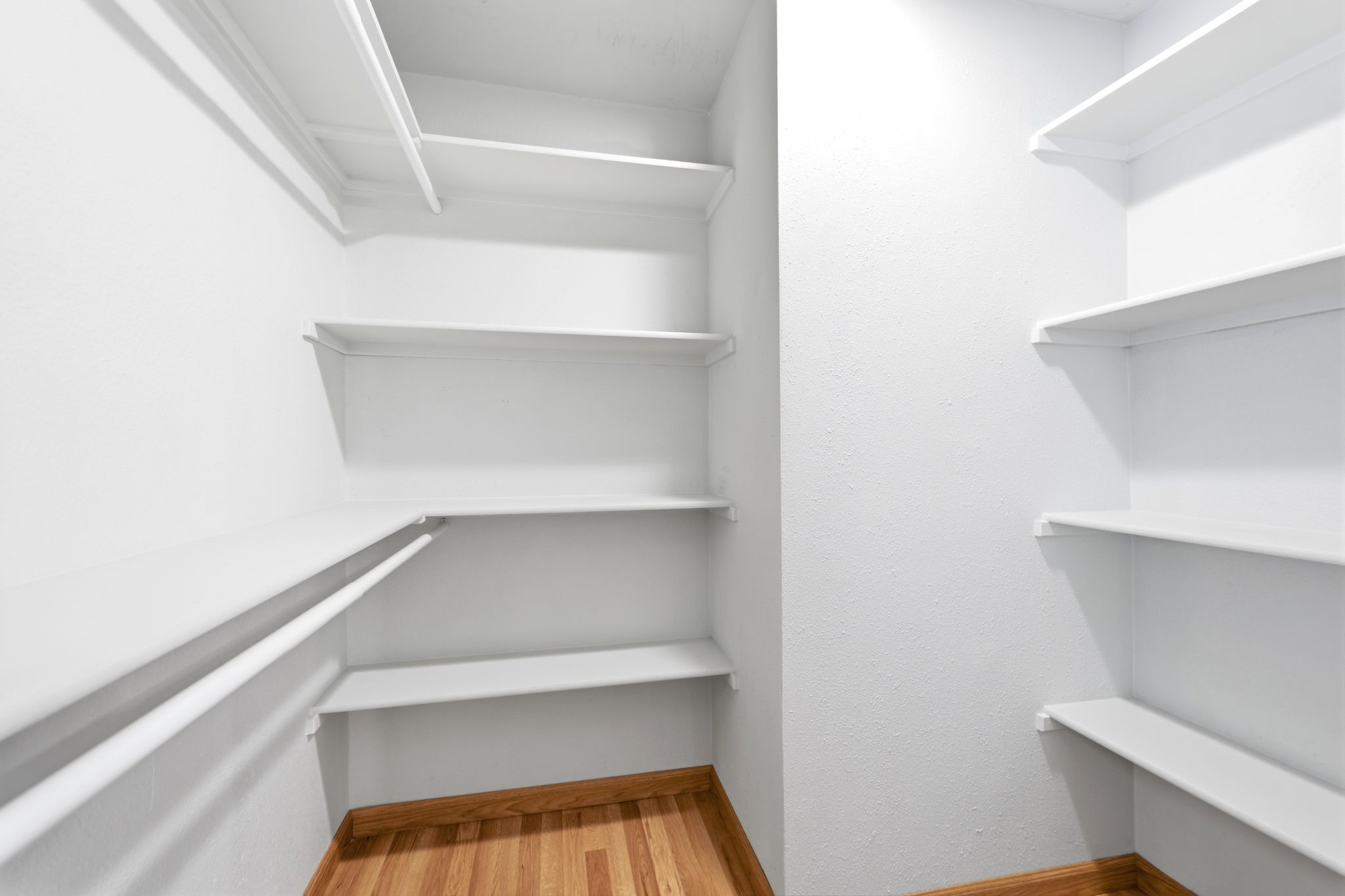 Walk-in closet with extensive white shelving, multiple hanging rods, and wood-finish flooring