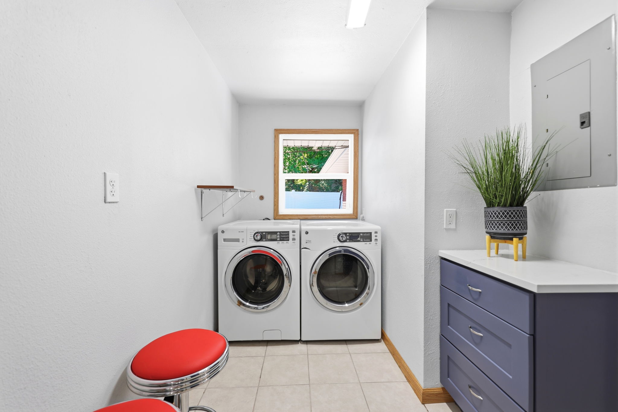Laundry room featuring tile flooring, a wood-framed window, a built-in countertop, and cabinetry with drawer storage