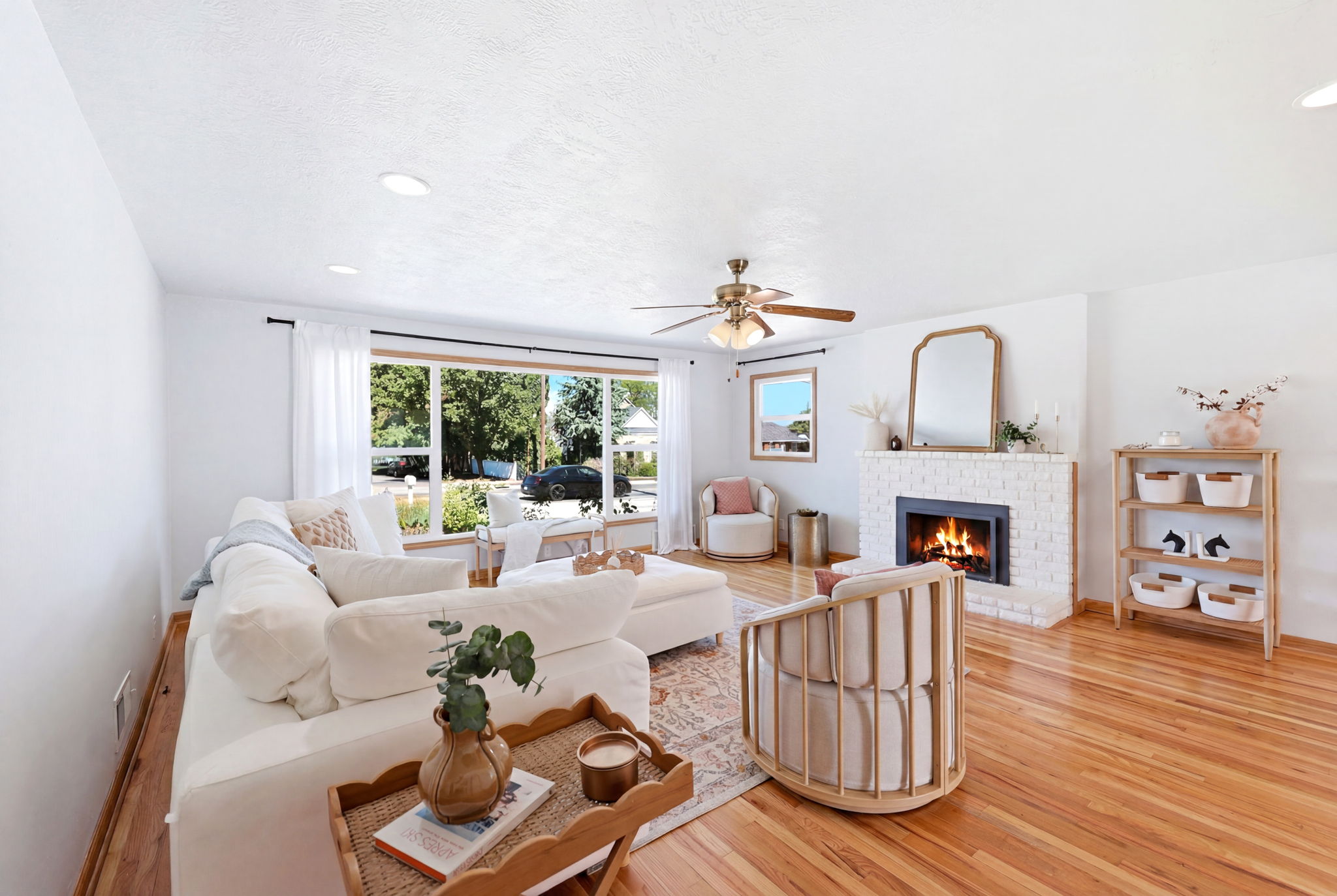Spacious living area featuring expansive windows, wood-finish flooring, a white brick fireplace, recessed lighting, and a ceiling fan with integrated lighting