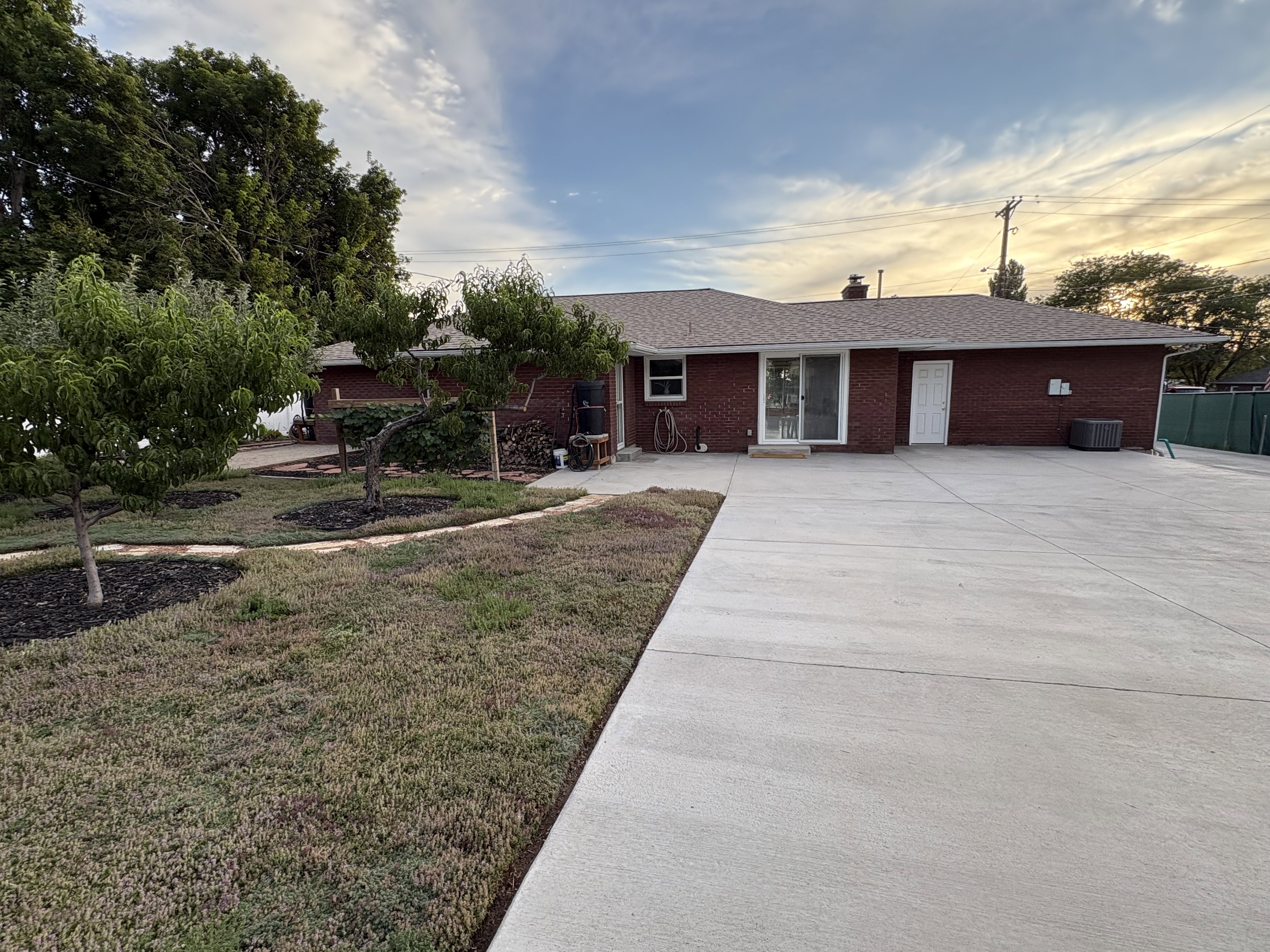 Brick exterior with a shingle roof, featuring mature trees and a substantial concrete patio