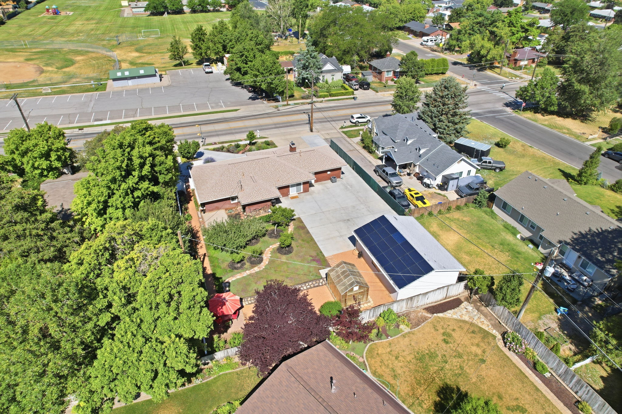 Aerial perspective showcasing a single-story residence with a paved driveway and an adjacent structure featuring solar panels