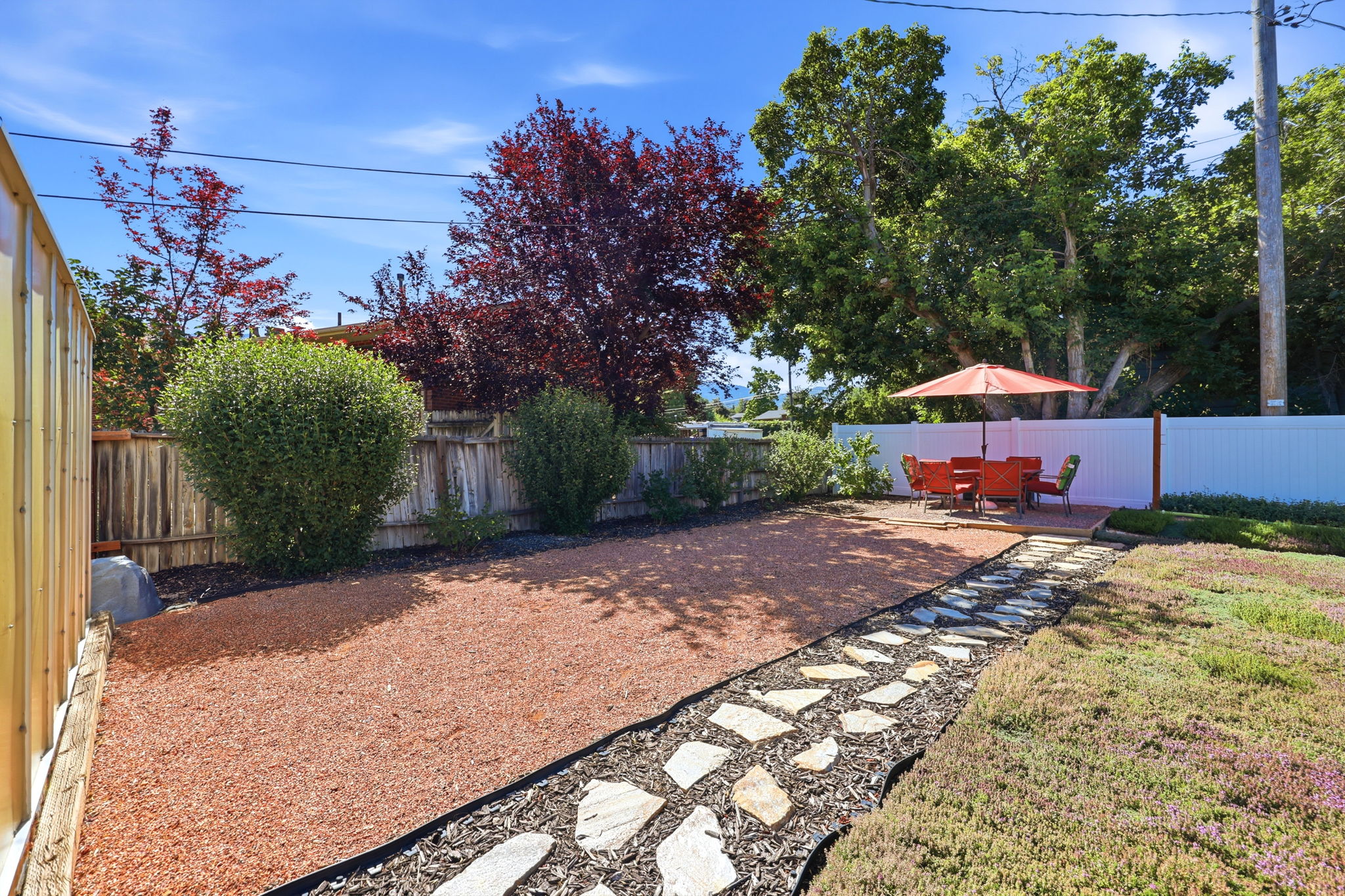 Landscaped backyard featuring an irregular flagstone pathway, a red gravel area, and a private wooden deck