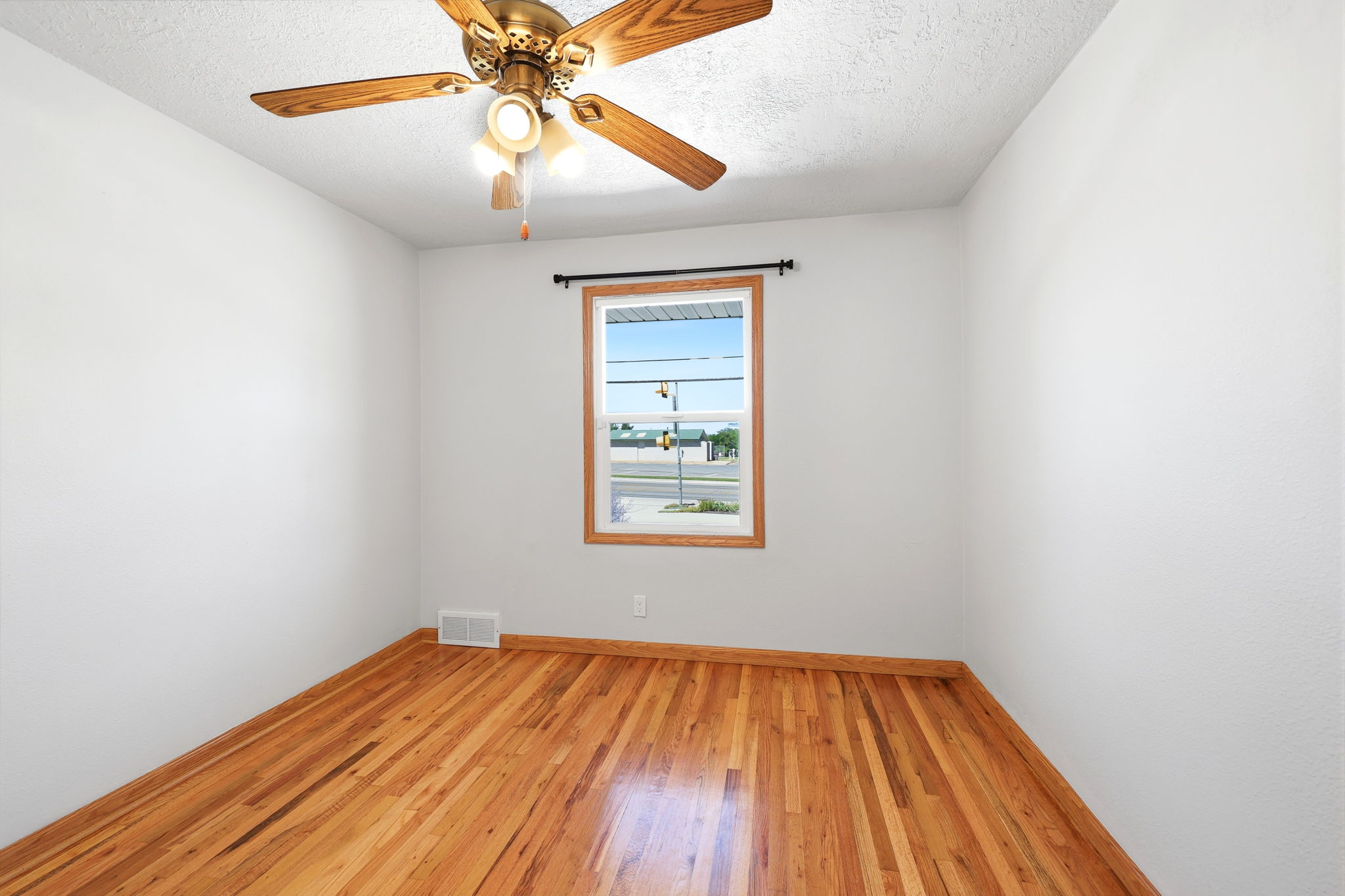 Bright room featuring wood-finish flooring, white walls, and a ceiling fan with integrated lighting