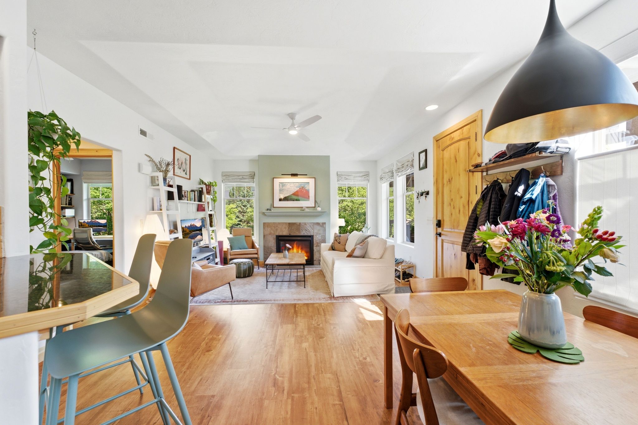 Open-concept living area featuring wood-finish flooring, a stone-clad fireplace with a light green mantel, recessed lighting, and multiple windows