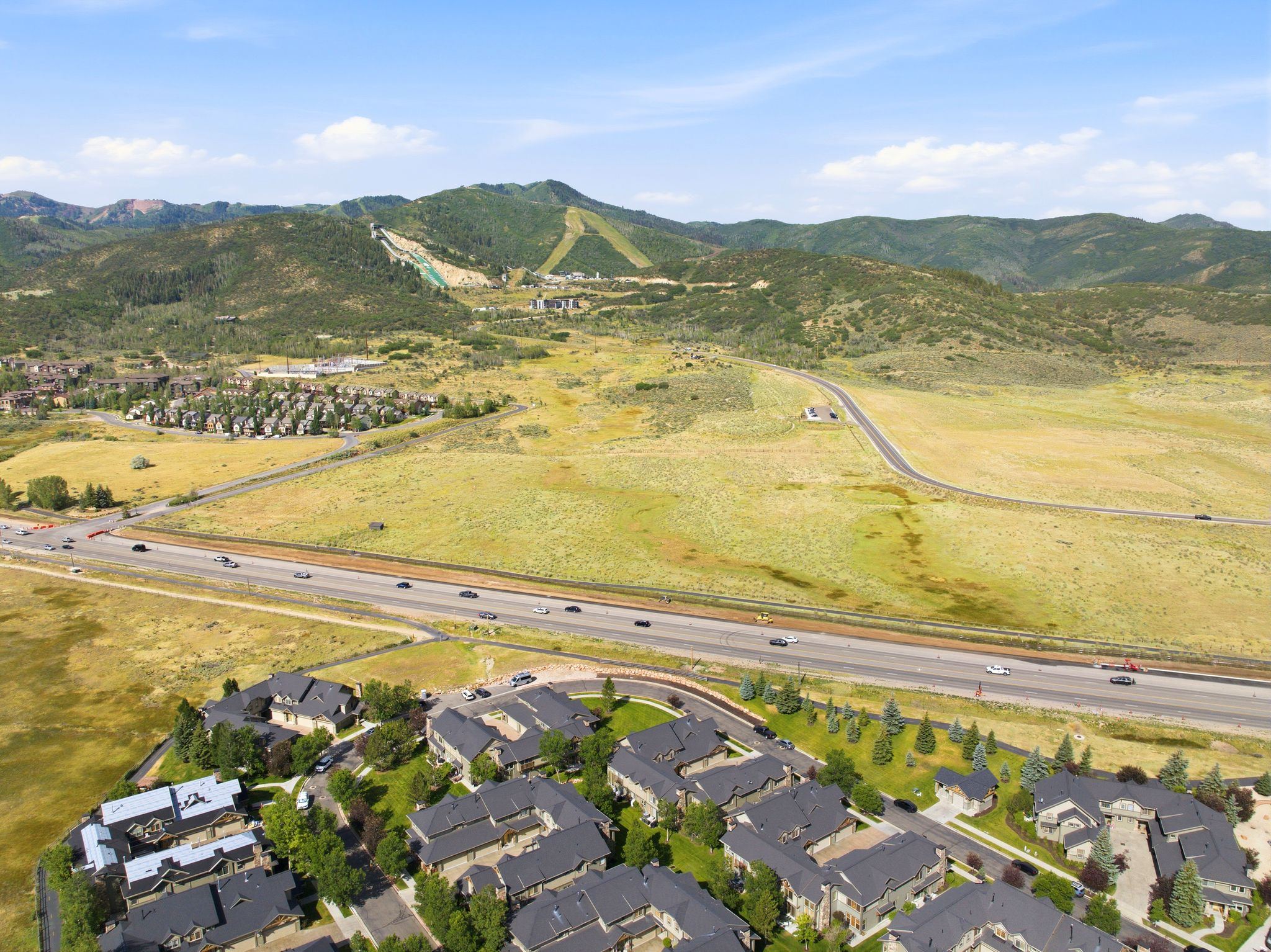 Expansive mountain landscape featuring a valley with a highway, residential developments, and distant ski slopes