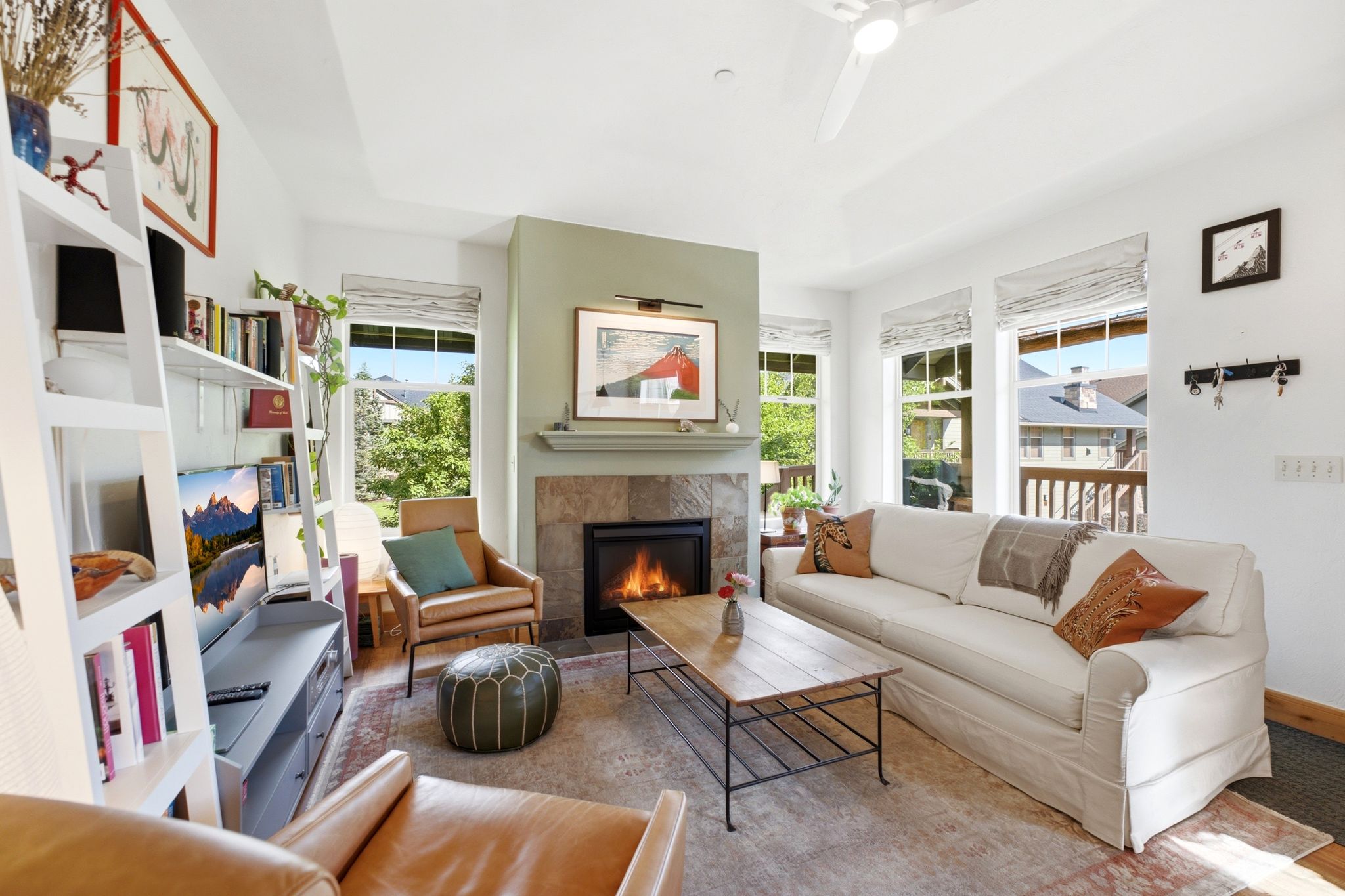 Living area featuring a tiled fireplace with mantel, multiple large windows, a tray ceiling, and built-in shelving
