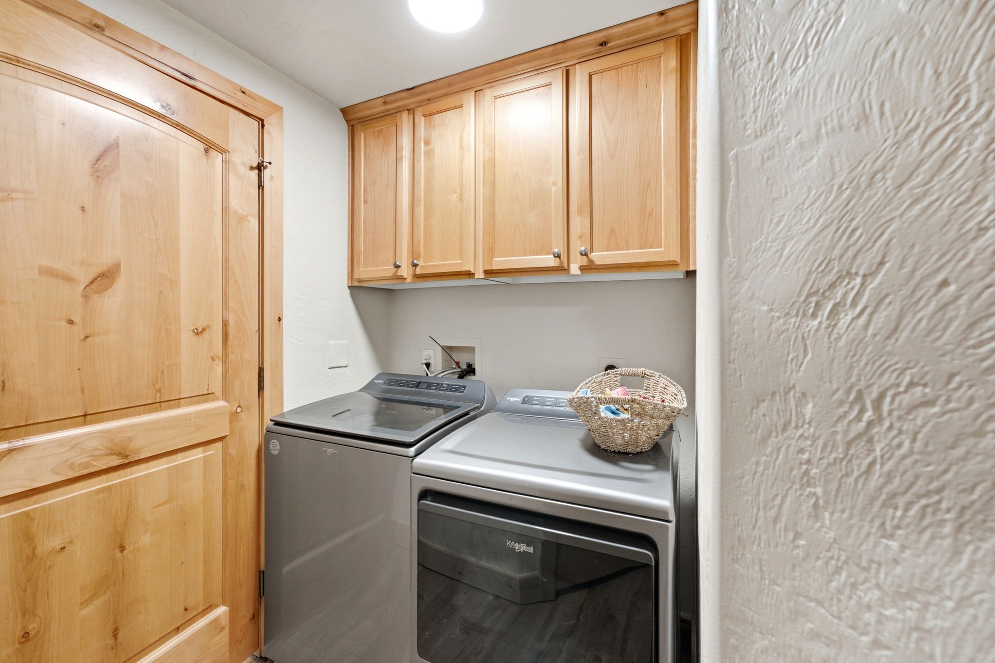 Dedicated utility space featuring light wood cabinetry, recessed overhead lighting, textured wall finish, and a natural wood door