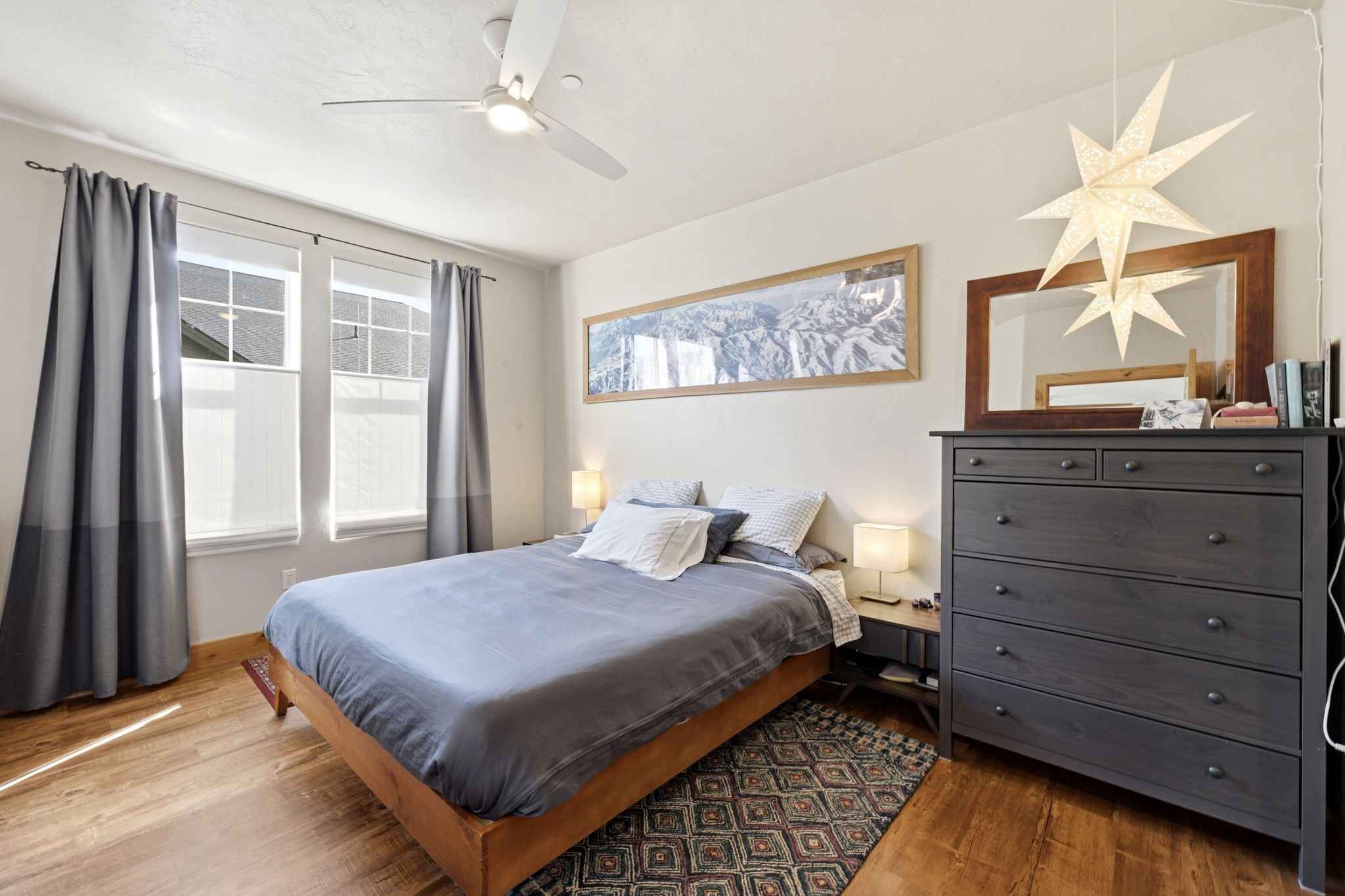 Room featuring wood-finish flooring, two large windows, and a ceiling fan with integrated lighting