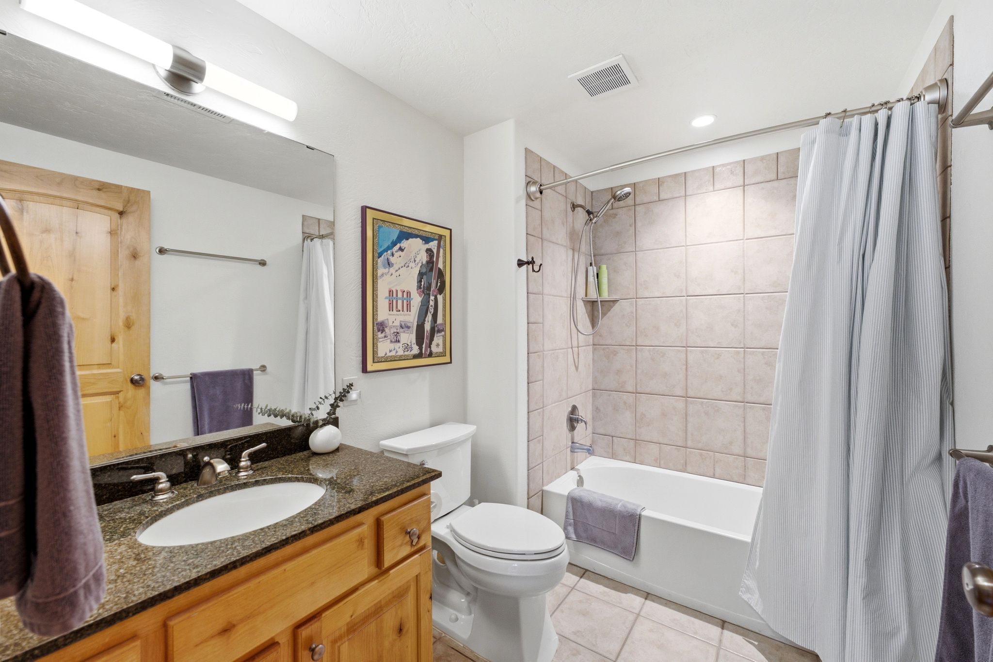 Bathroom featuring a wood-finish vanity with a dark granite countertop, an undermount sink, and a large mirror